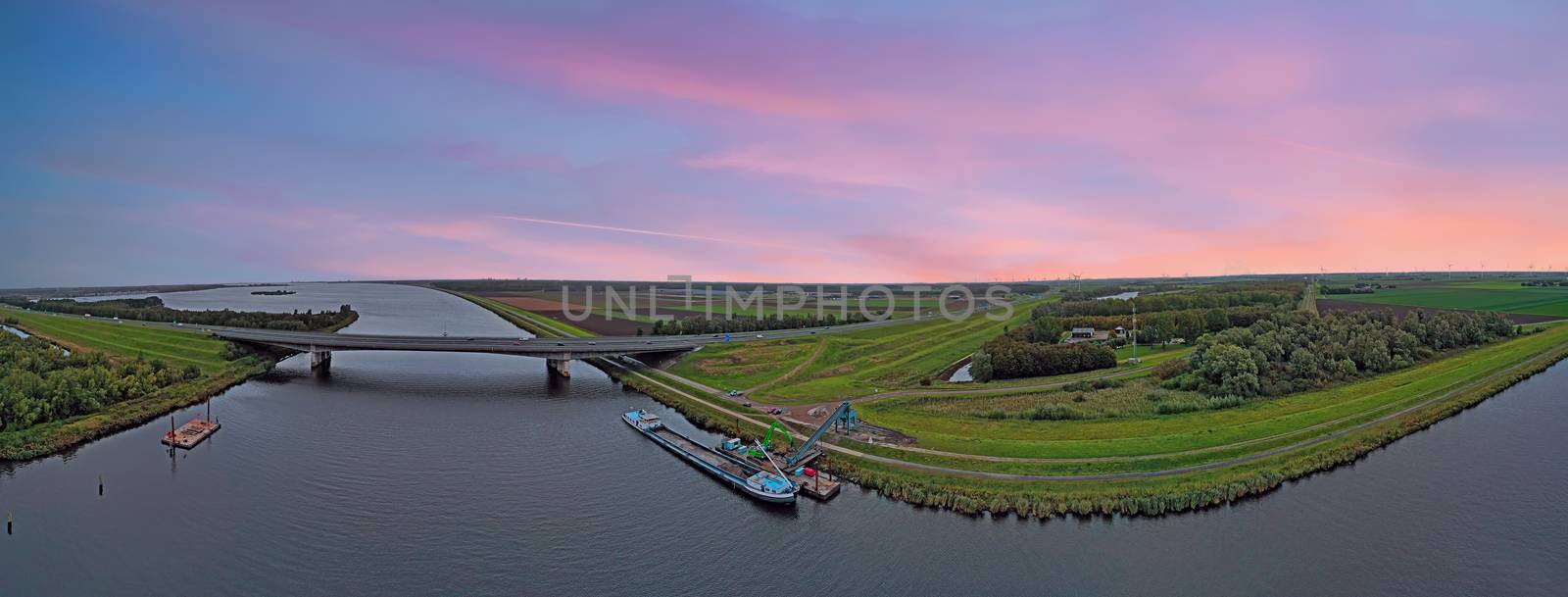 Typical dutch panoramic scenery at sunset: Highway A1 and a freighter unloading in the countryside from the Netherlands