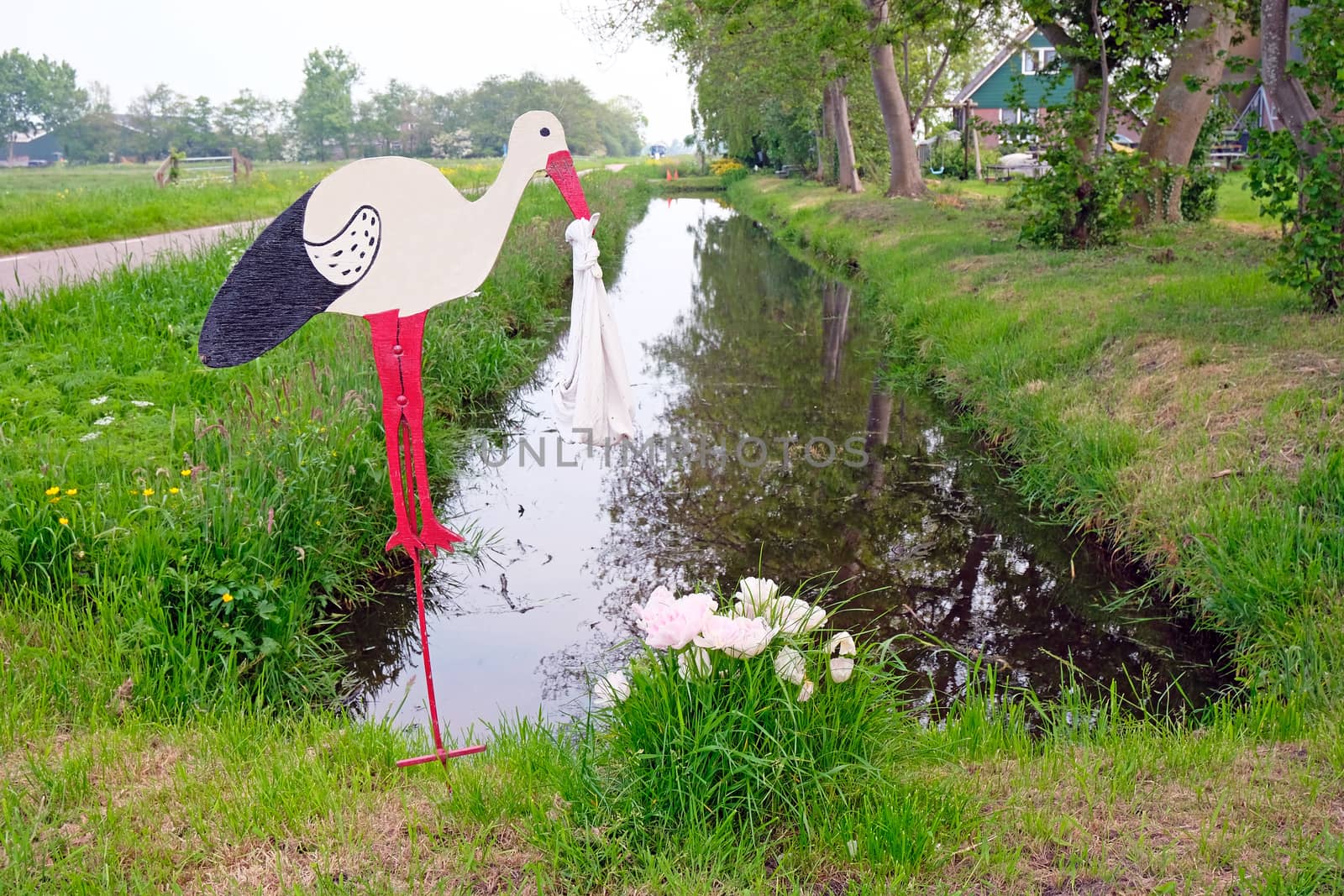 Design of a stork bringing a baby to a house in the countryside of the Netherlands