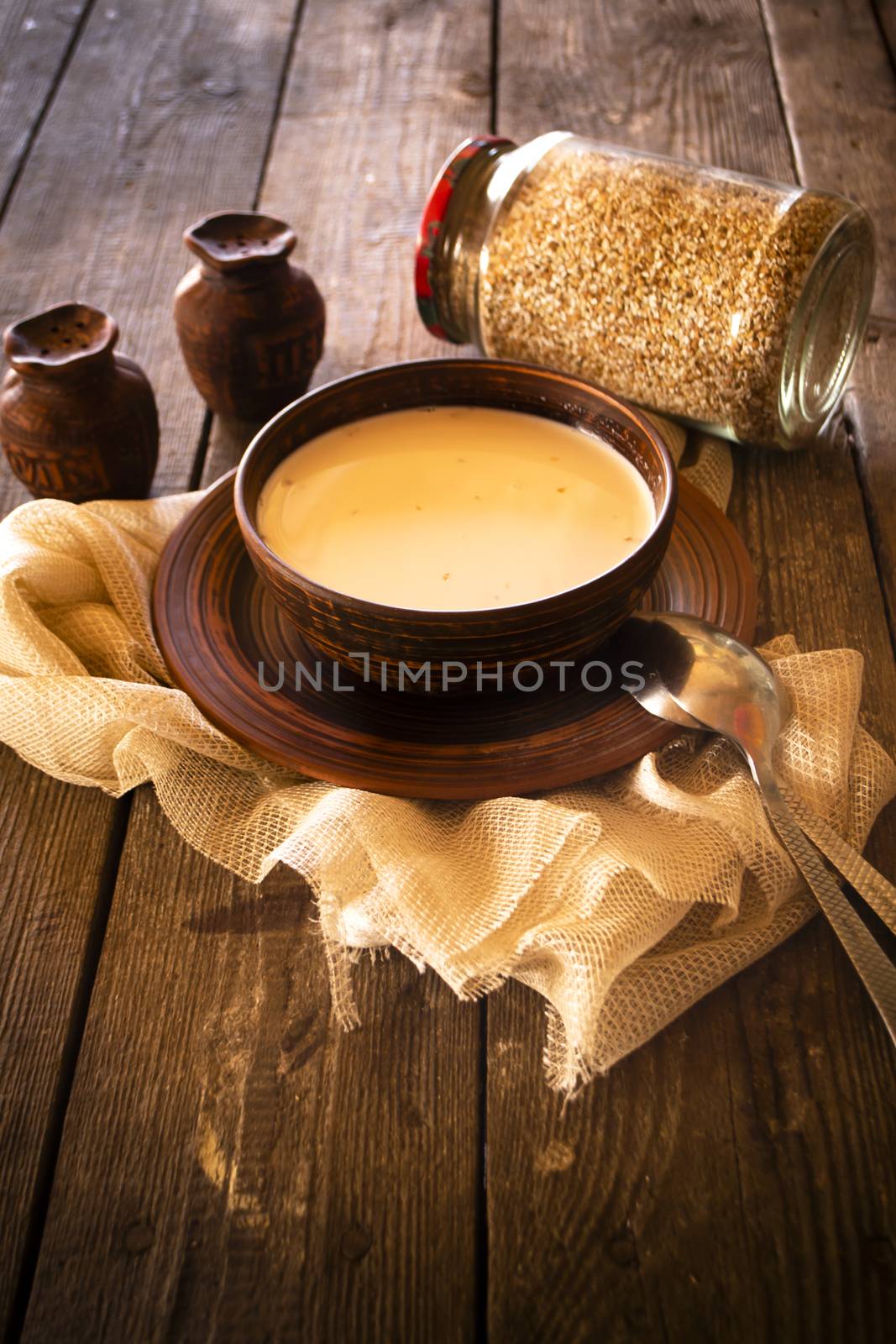 Boiled buckwheat with milk in wooden bowl on rustic wooden table, vertical