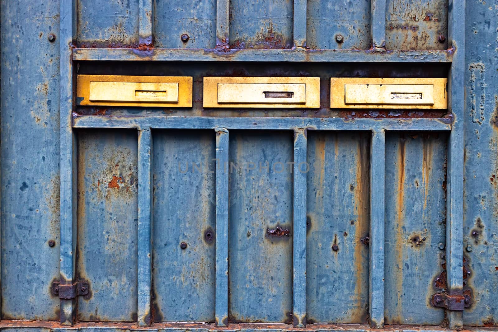 Rusty metallic door with three golden mail boxes 