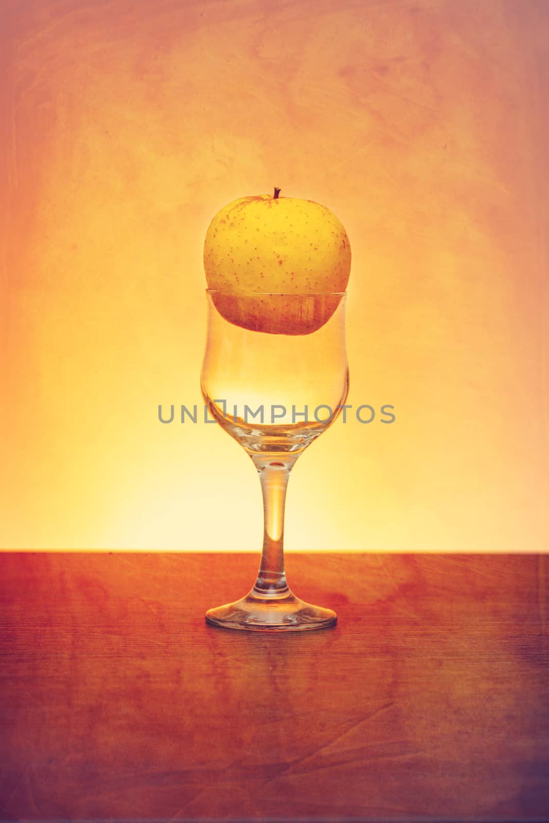 Conceptual idea of golden apple in the cider glass as raw material instead of  final product using retro filter