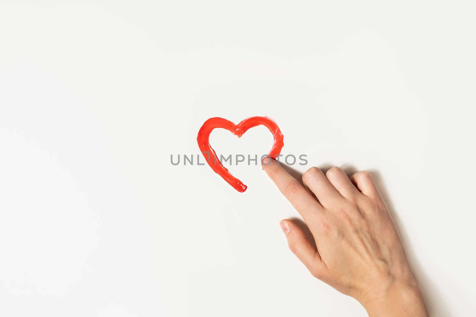 Finger draws a heart's shape with red paint on a white background. Charity, love or St. Valentines day concept.