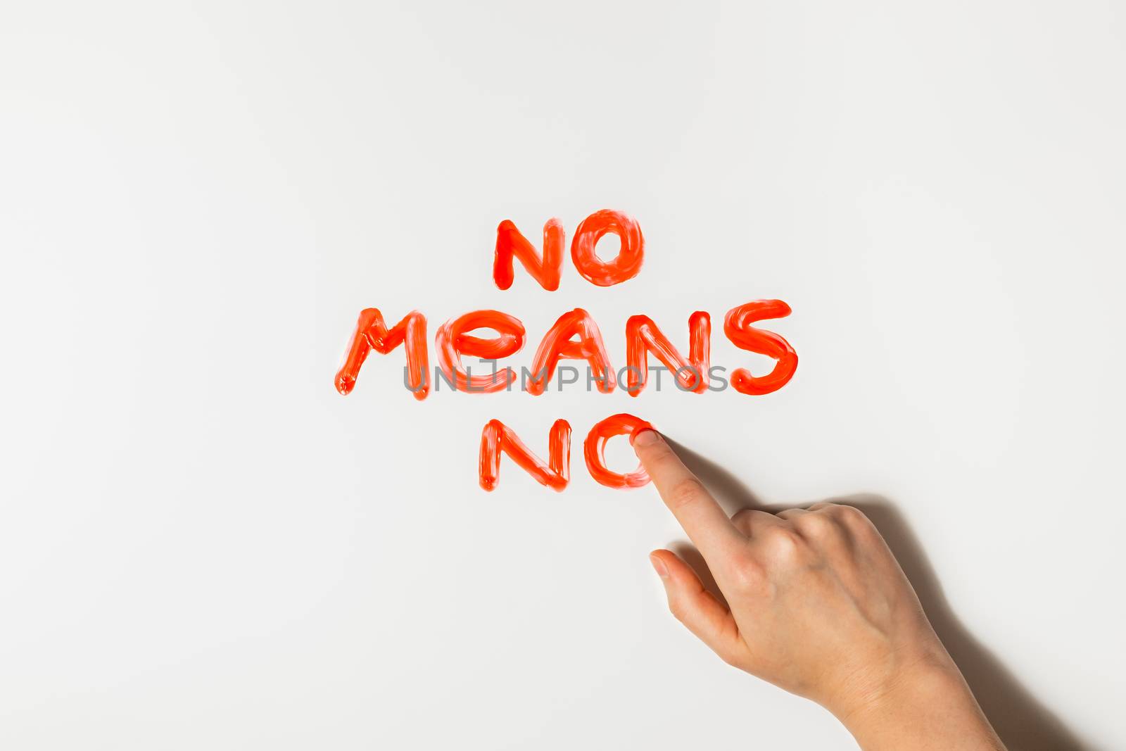 Women finger draws a phrase "No means no" with red paint on a white background. Sexual abuse, rape prevention and personal boundaries concepts.
