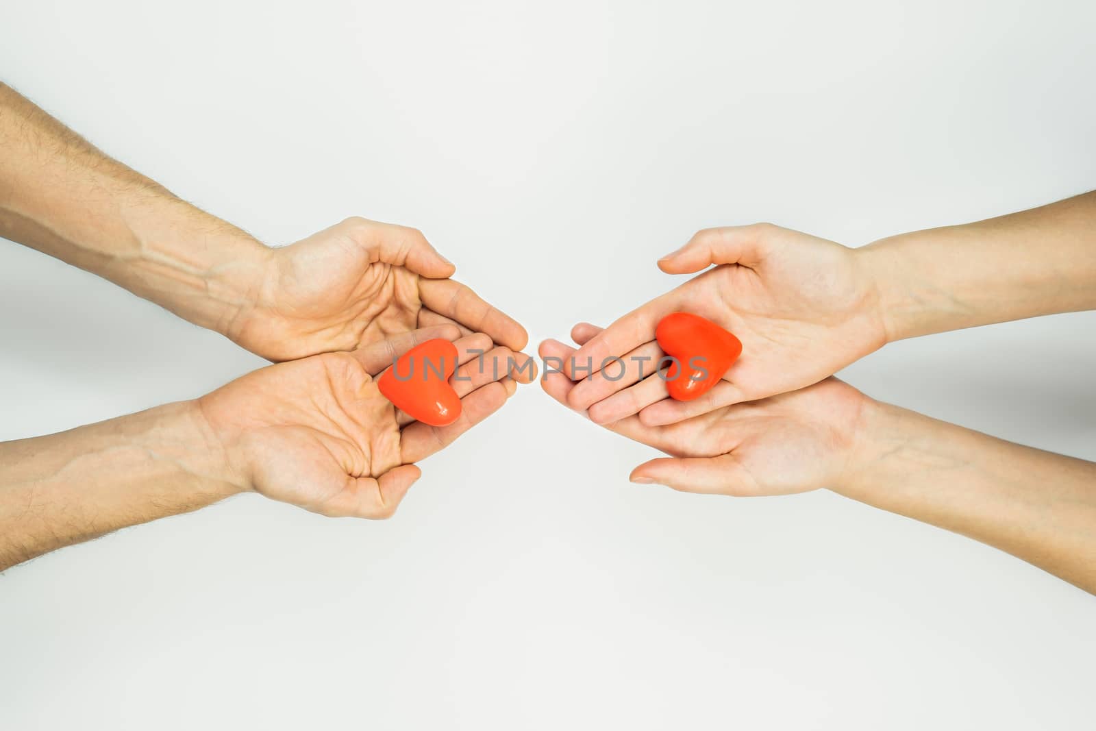 Female and male hands hold heart figures in palms on white background with copy space. Concept of charity, couples , relationships, love. St. Valentine's day concept