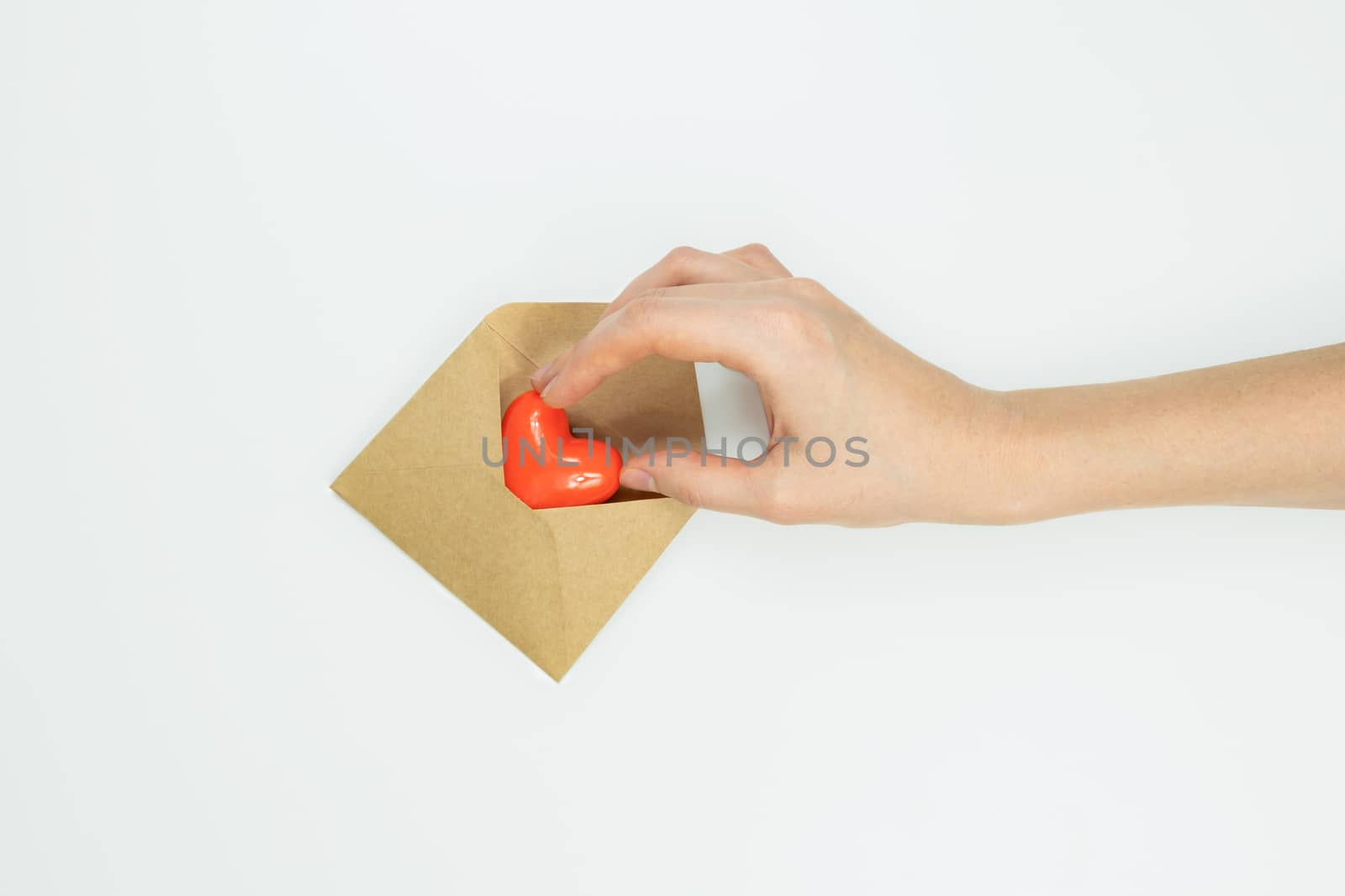 Hand puts heart figure in a letter envelope on white background, by photoboyko