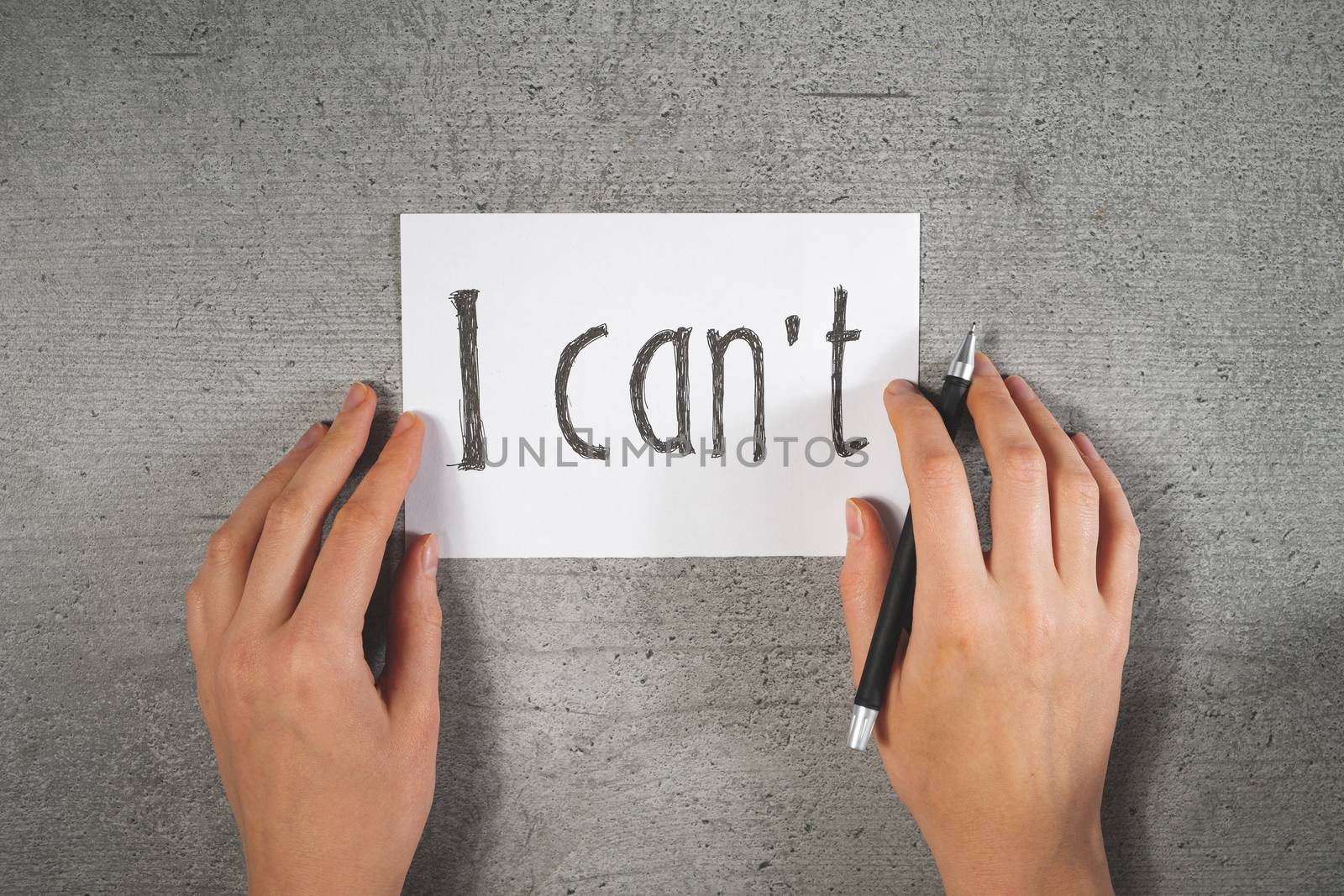 Hands with a pen and sign "i can't" on the paper. Motivational concept, writing a note, disbelief in yourself or lack of self confidence concept.