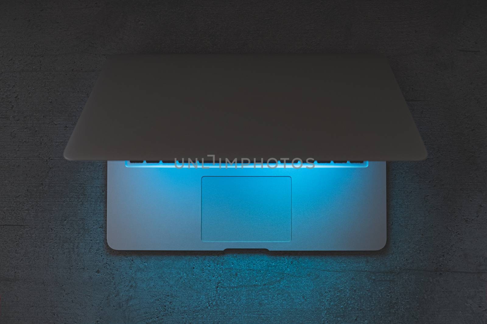 Top view of a laptop on a dark table, glowing blue screen. Minimalistic workplace, working with computer, using laptop at night and online privace concept