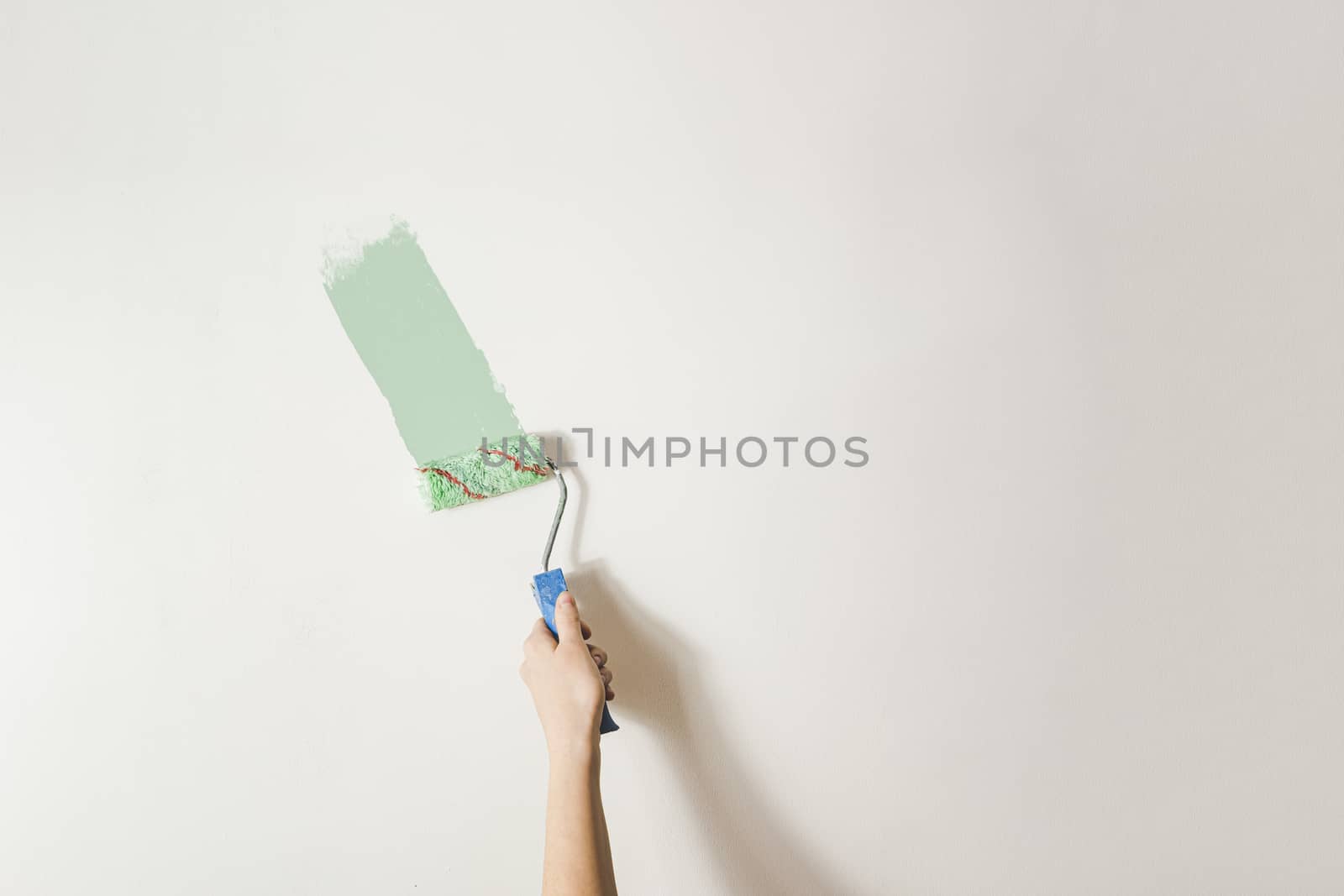 Hand with a paintbrush against the white wall. by photoboyko