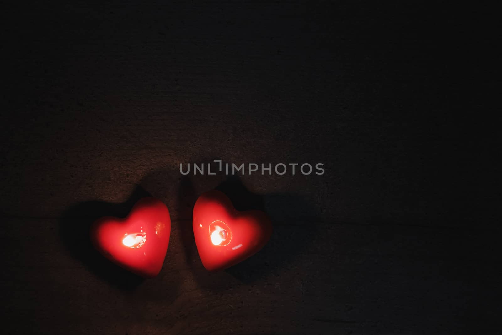 Two heart shaped candles burn in the darkness, top view by photoboyko