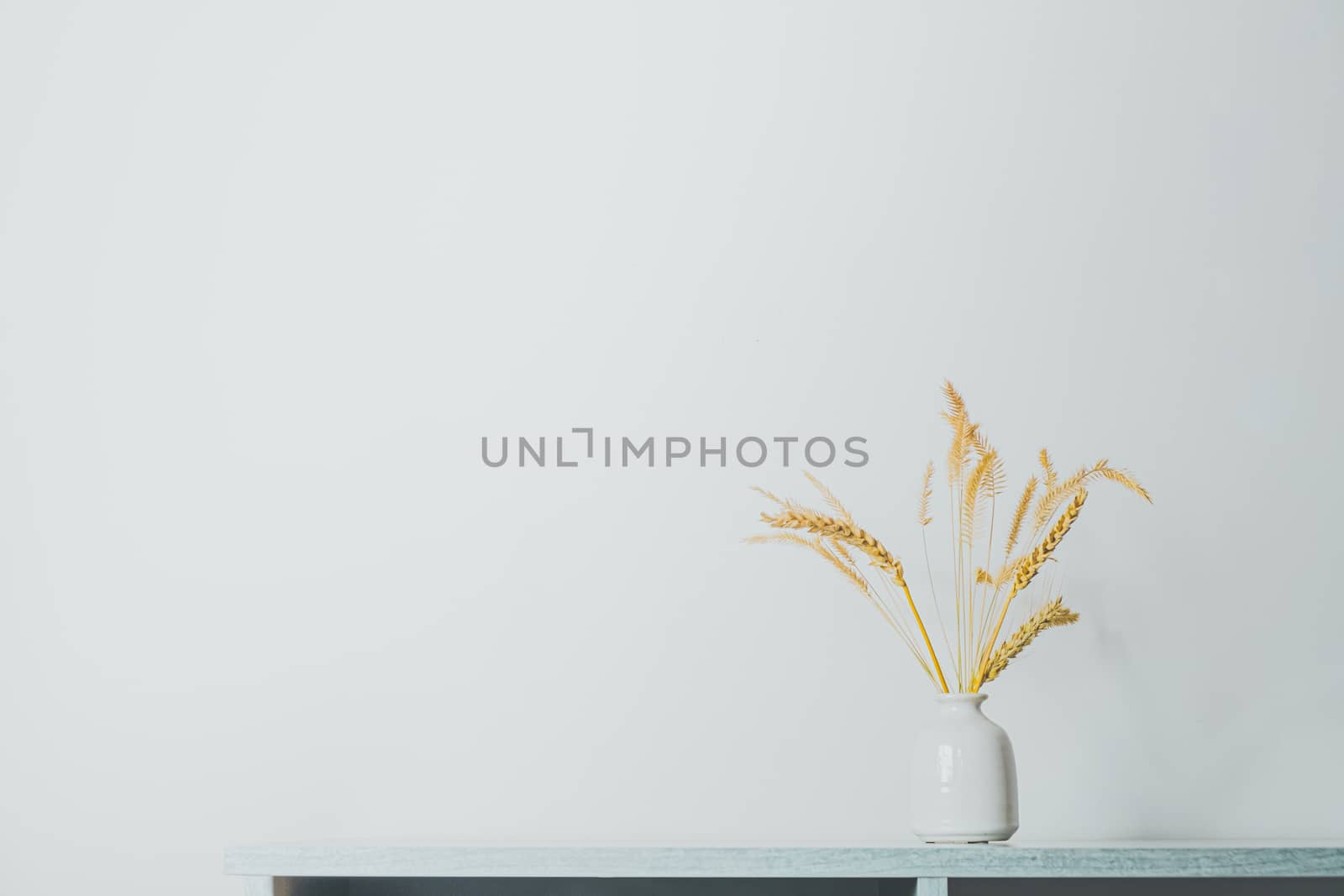 Spikelets or wheat in a vase on the table. Home decoration elements in sparse pastel background