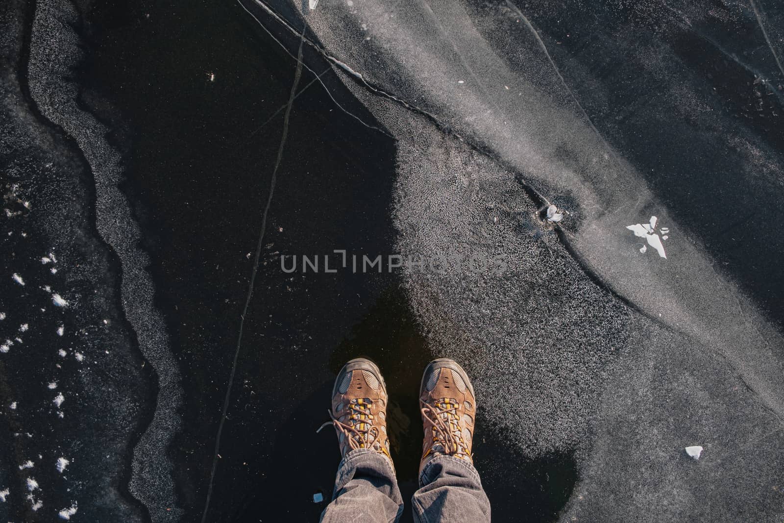 Standing on the thin ice, top view. Human feet on beautiful textured ice on the lake or river