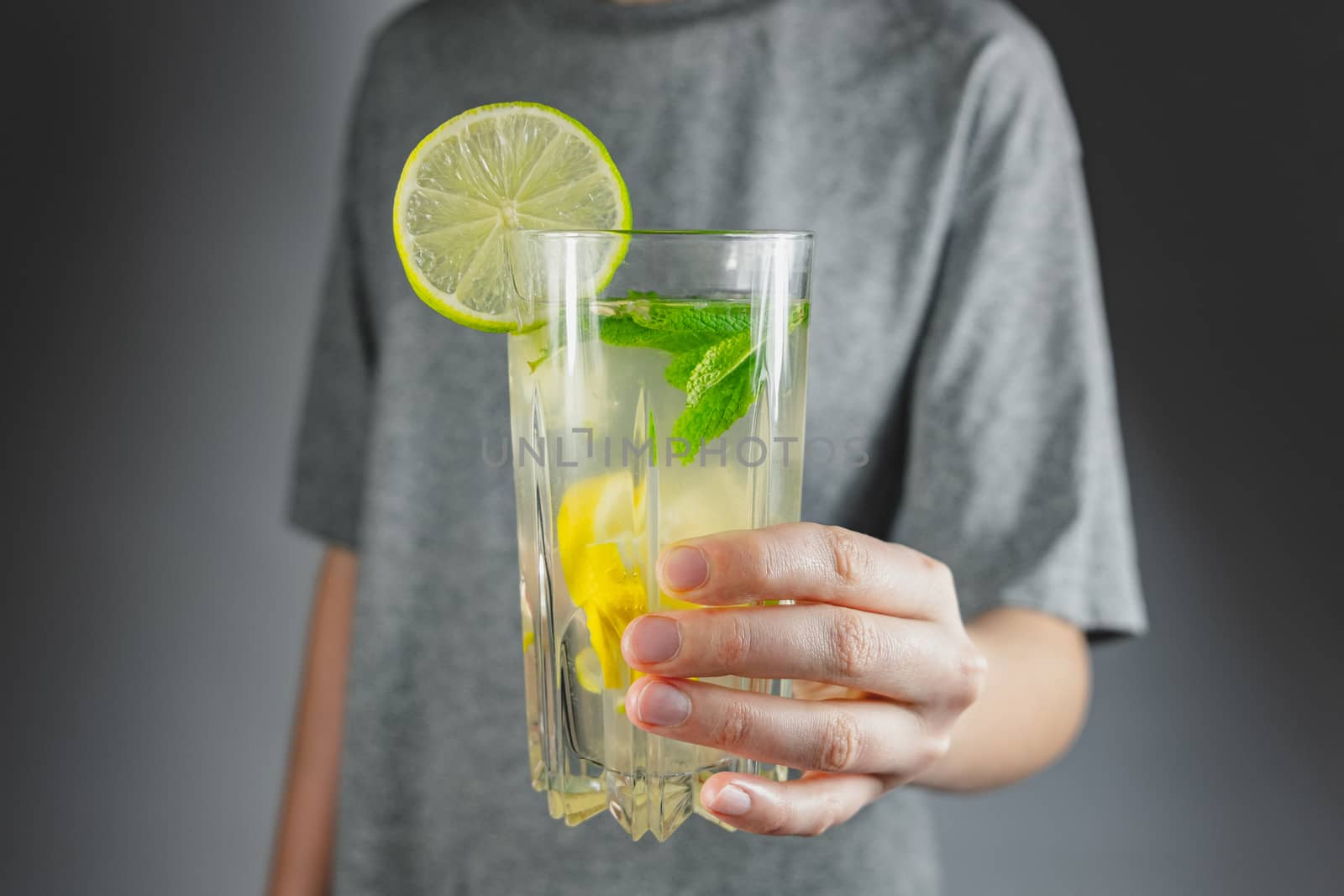 Glass of lemon drink in a human hand. Hangover cure, tonic water or mojito refreshment