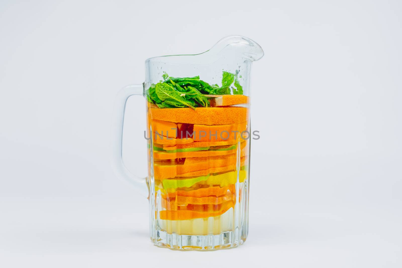 Large glass jar with citrus fruit and mint in white background. Lemonade with oranges, lime and lemons. Healthy and vitamins rich fruit drink