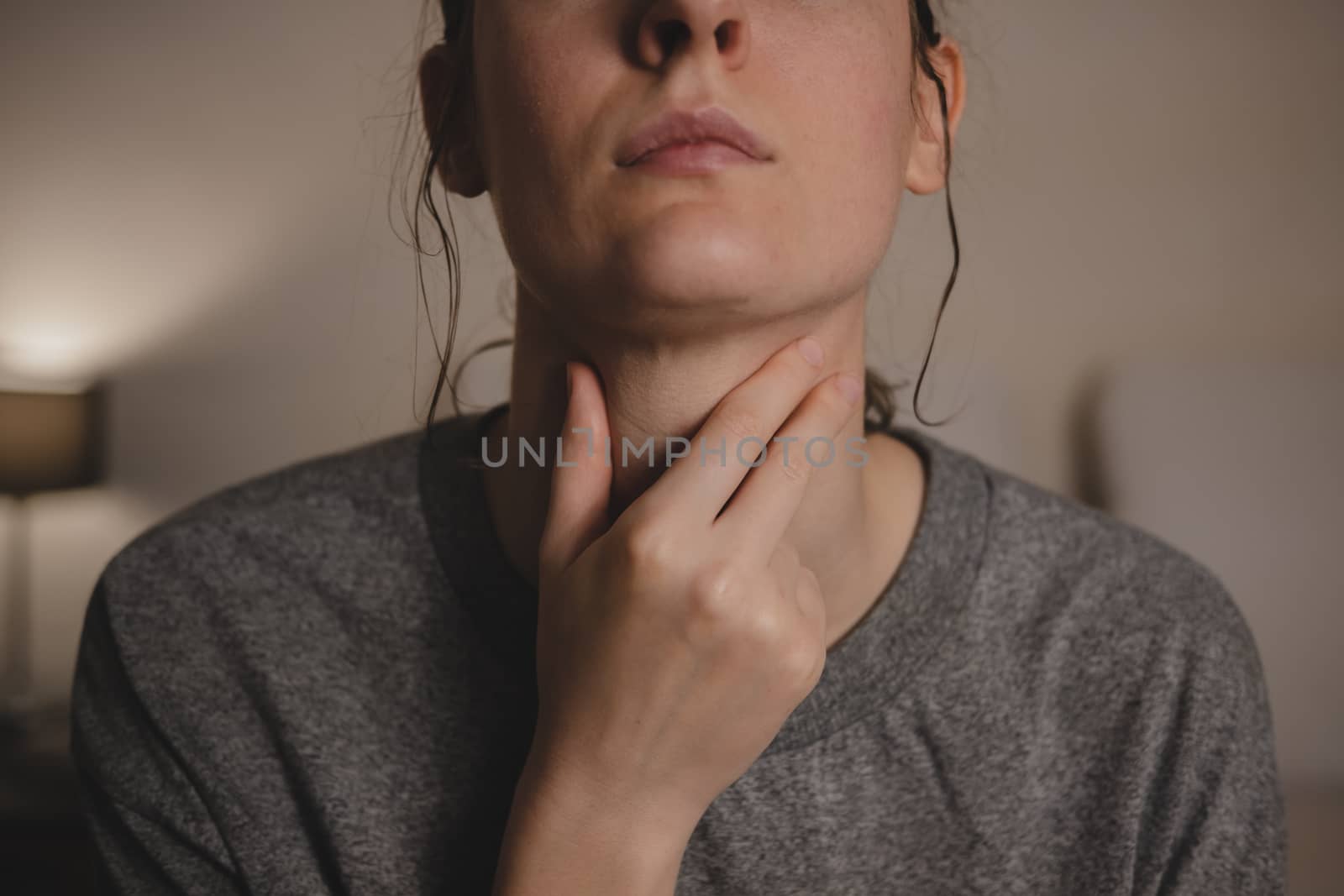 Sore throat, virus disease or flu. Woman holds hand against her throat feeling pain in bedroom