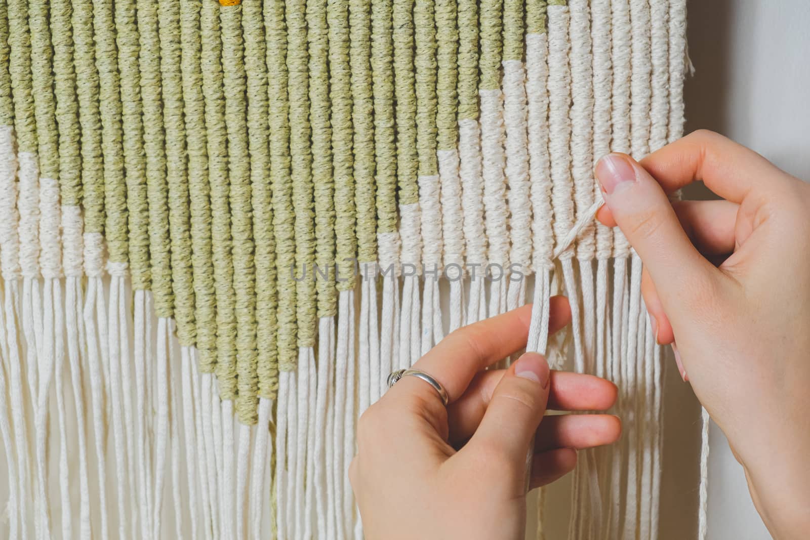 Hands doing macrame craft. Hand-making a cotton rope wall-hanging decor piece, concept of handicraft hobby or handworking