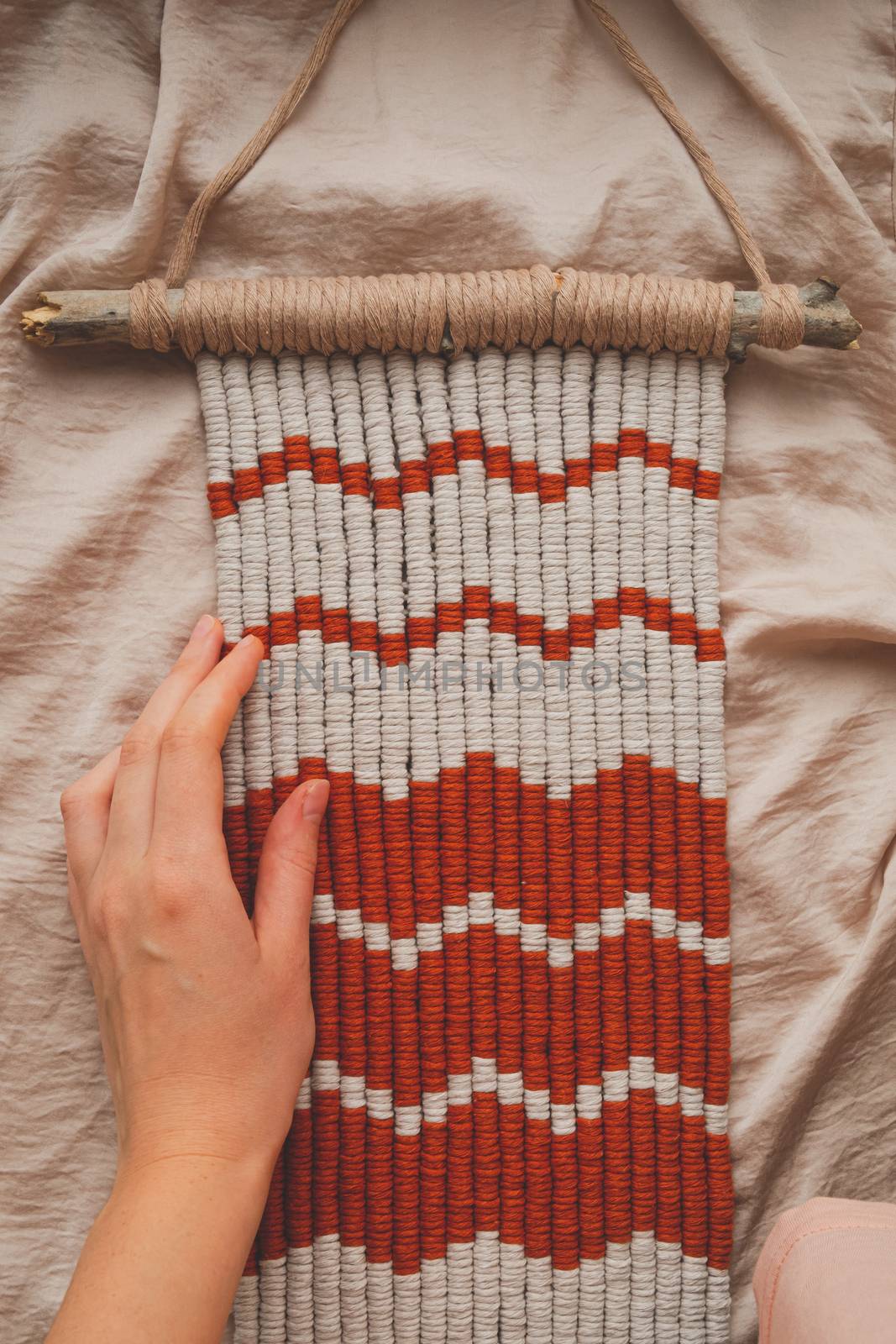 Handcrafted macrame wall hanging, close-up view. Human hand touches a handcrafted piece of decor