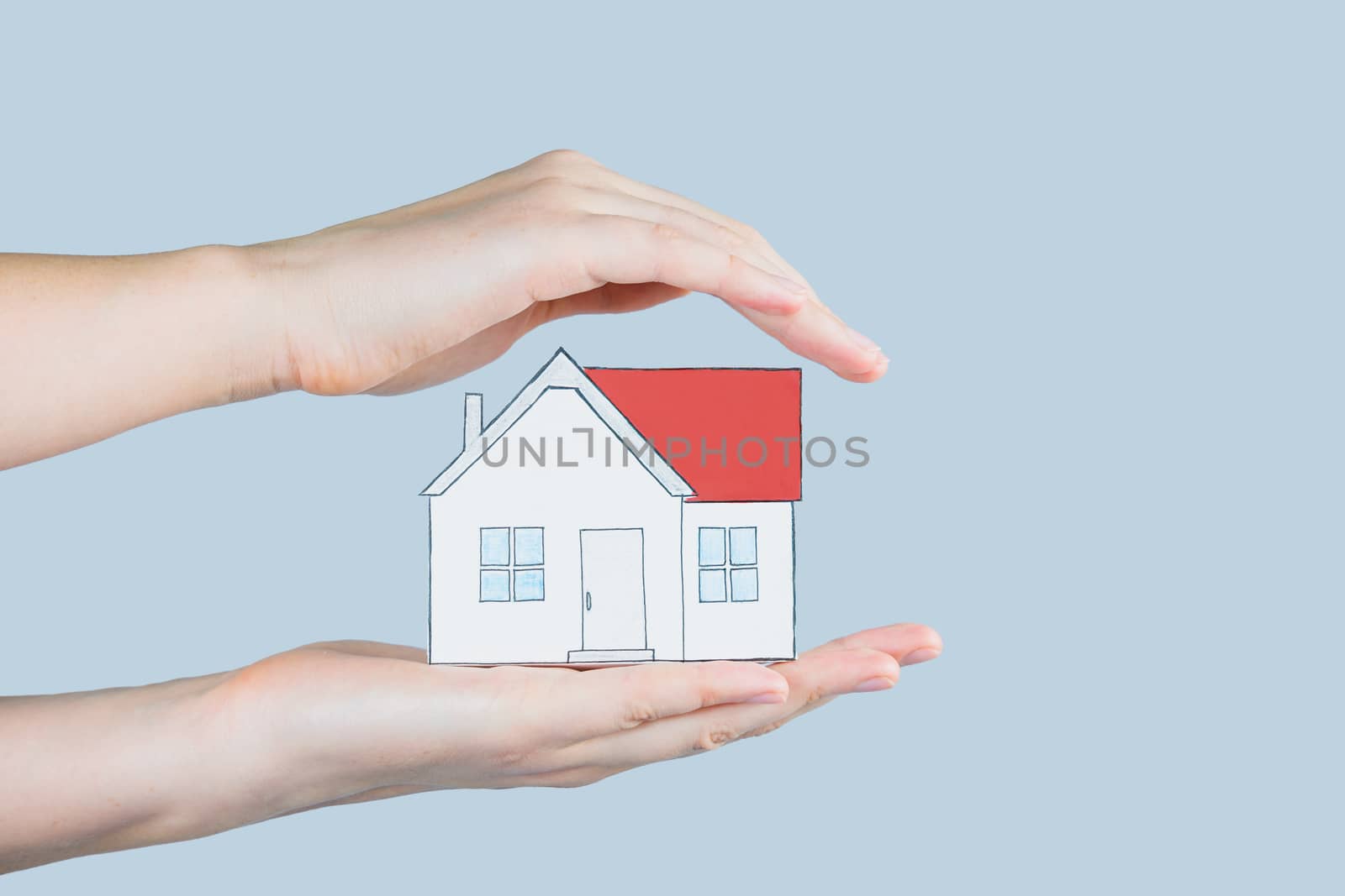The figure of a house in human hands. Hands hold and gently cover a figure of home - concept of home insurance, safety, family planning, mortgage and safe house