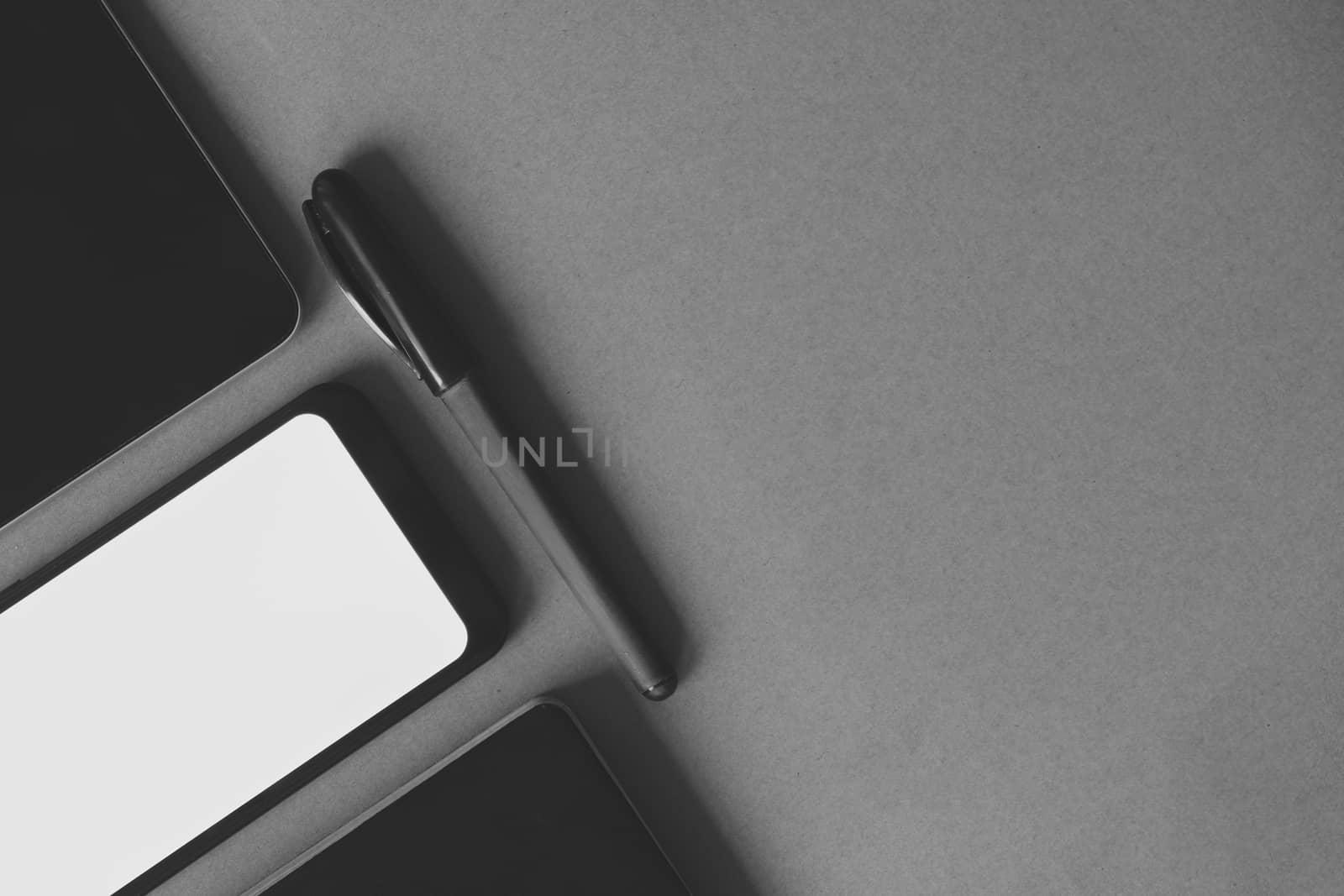 Business flat lay on dark paper background, monochrome image. Smartphone, tablet computer and notebook organizer on vintage background