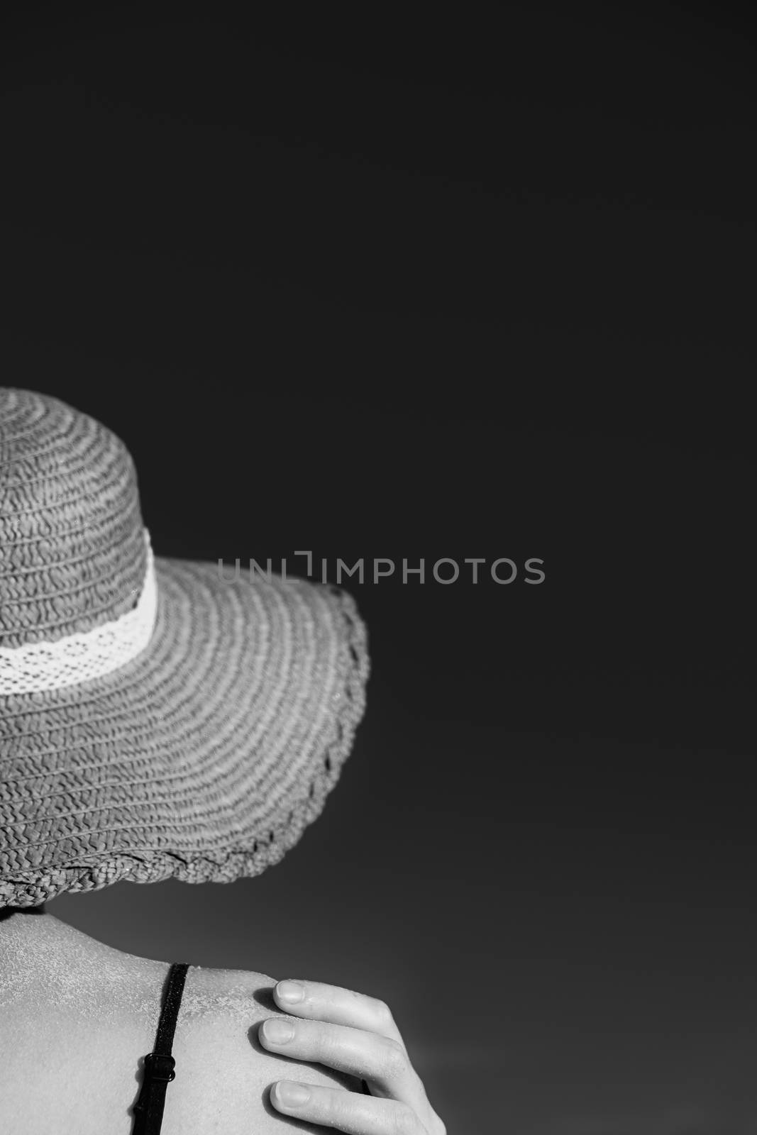 Summer holidays mood: female in beach hat, covered in sand in monochrome low key. Shoulders of a young woman in a retro hat, shot from behind