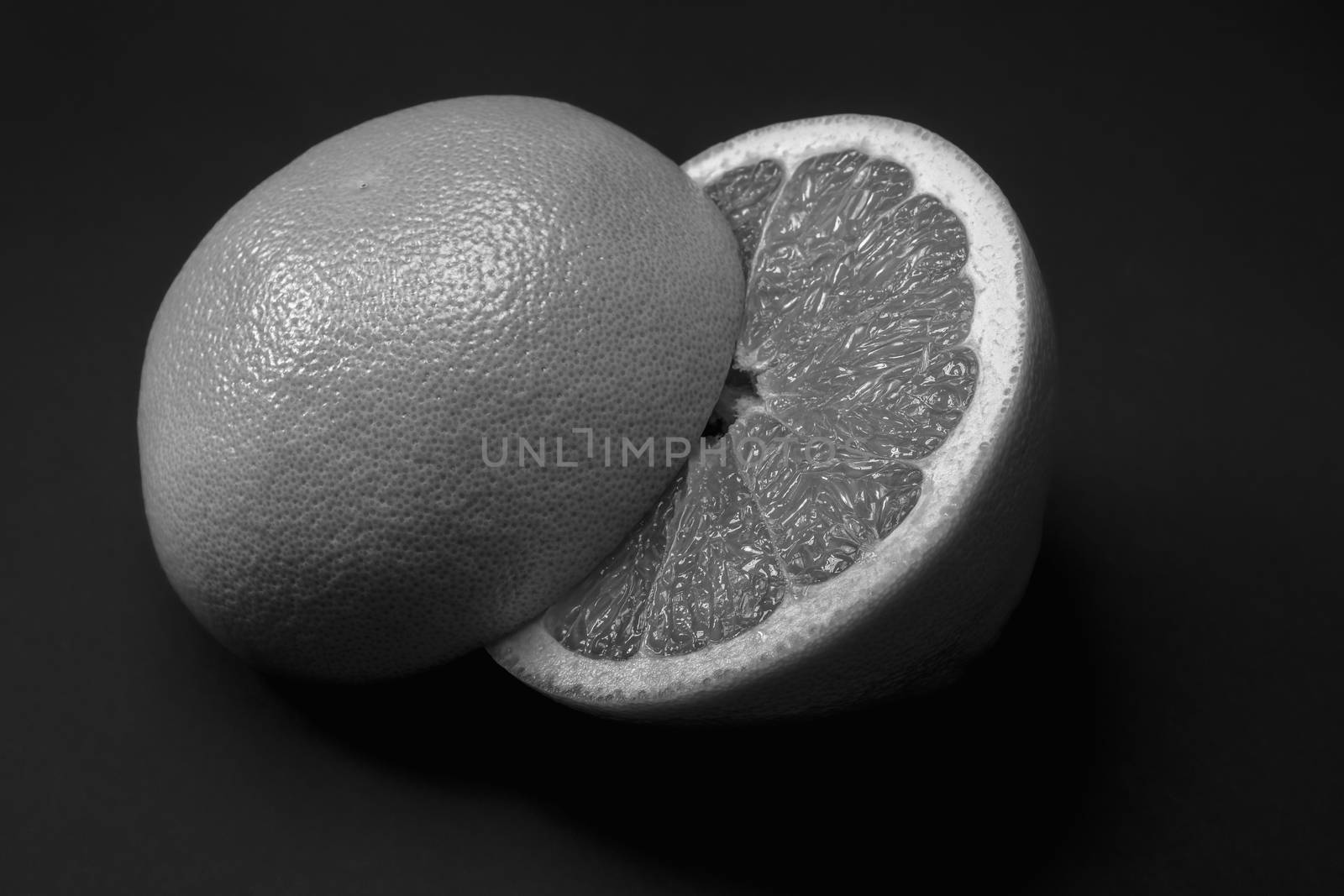 Grapefruit cut in half dark monochrome backdrop, copy space. Fruitarianism, vegetarian or vegan food: fresh and ripe citrus fruit in low key colors