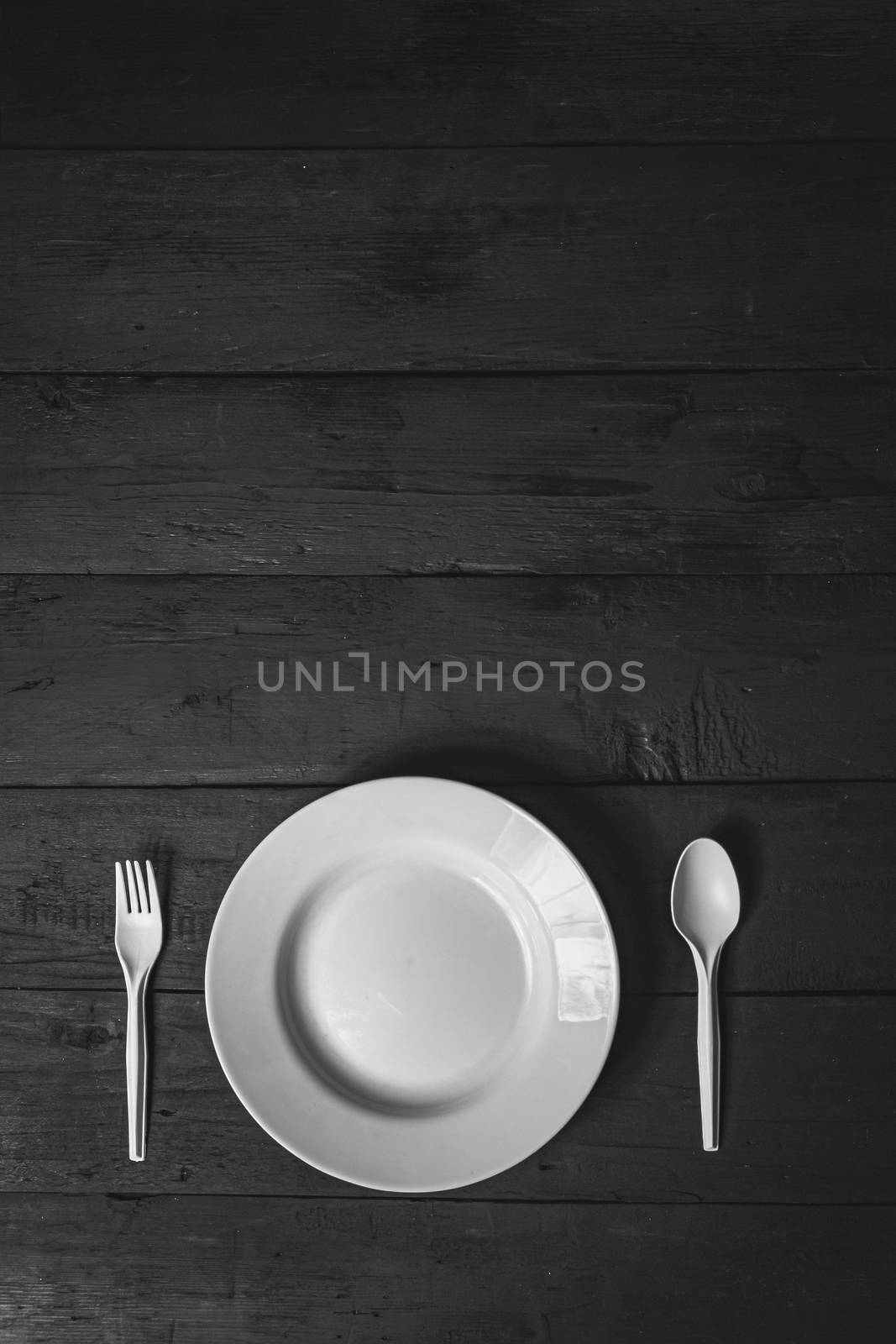 Empty white bowl, fork and spoon on black wood table, close-up view. Diet concept: flat lay of clean kitchen dishes on dark rustic background