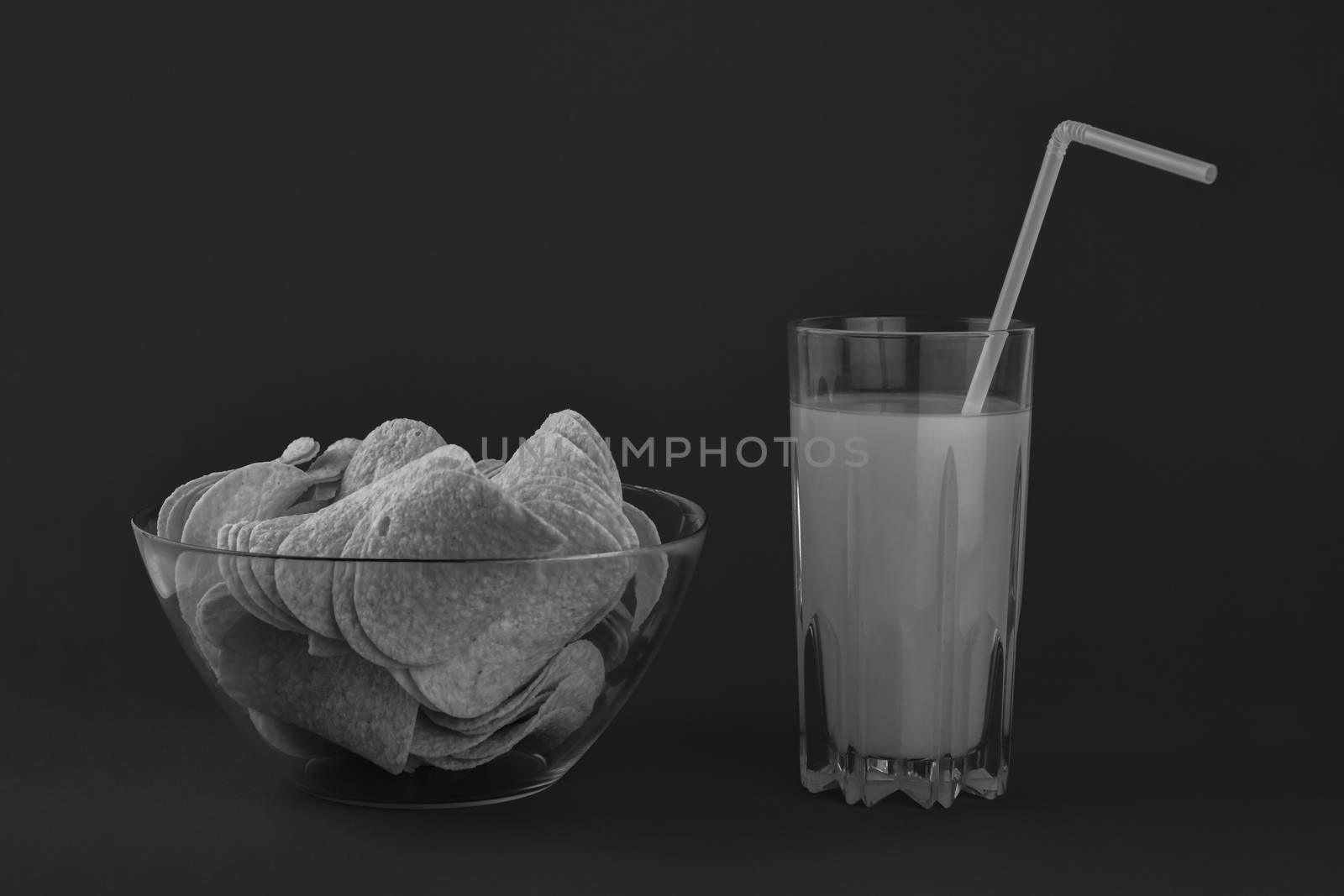 Bowl of potato chips and glass of orange drink in dark monochrome background. Minimalistic image of attention grabbing snacks and beverage