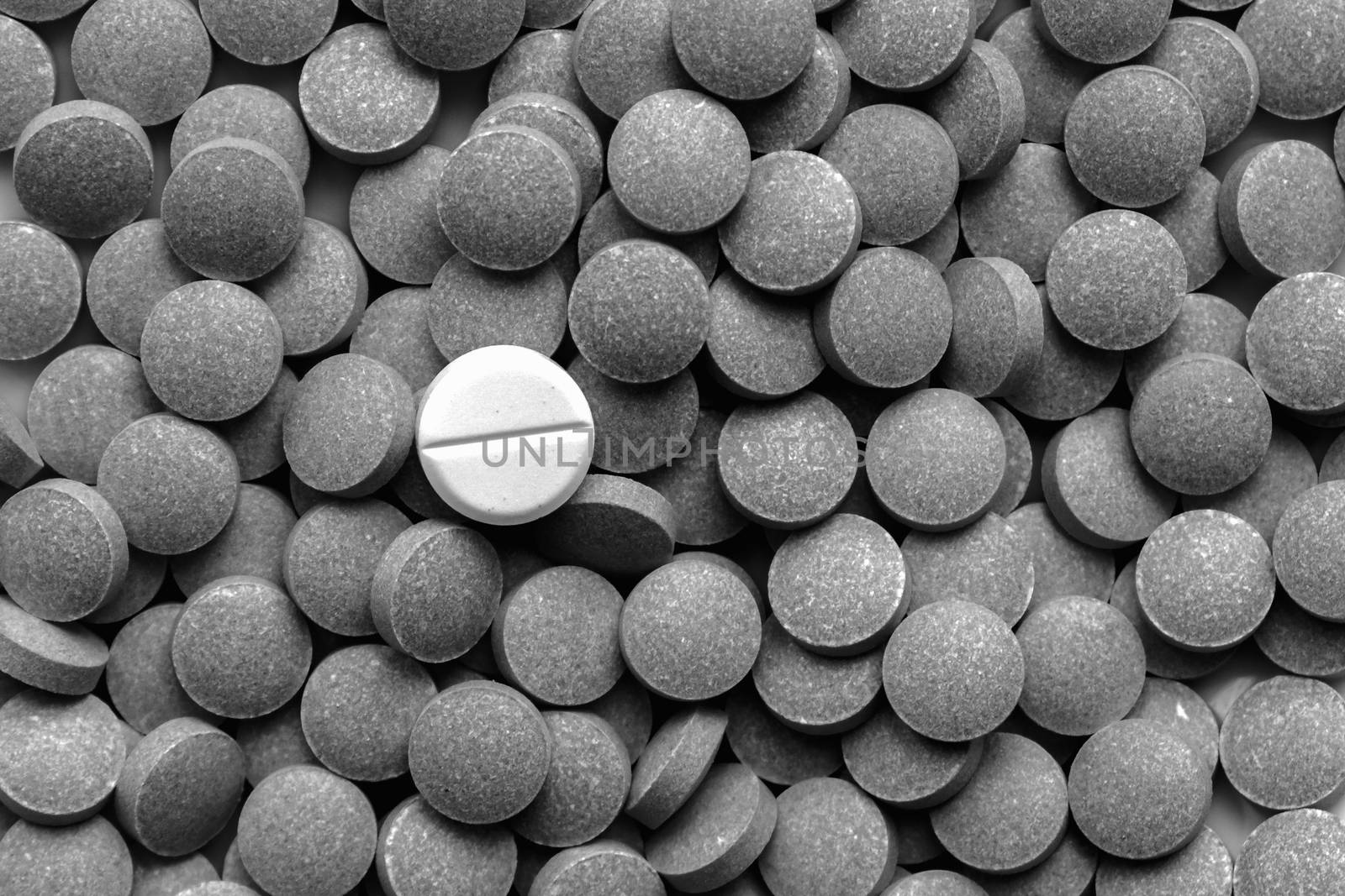 Pile of dark pills around a white one, low key monochrome. by photoboyko