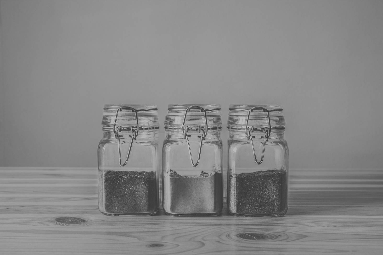 Jars with spices on light wood table, low-key monochrome. Three jars with eastern spices standing in row on light wood table