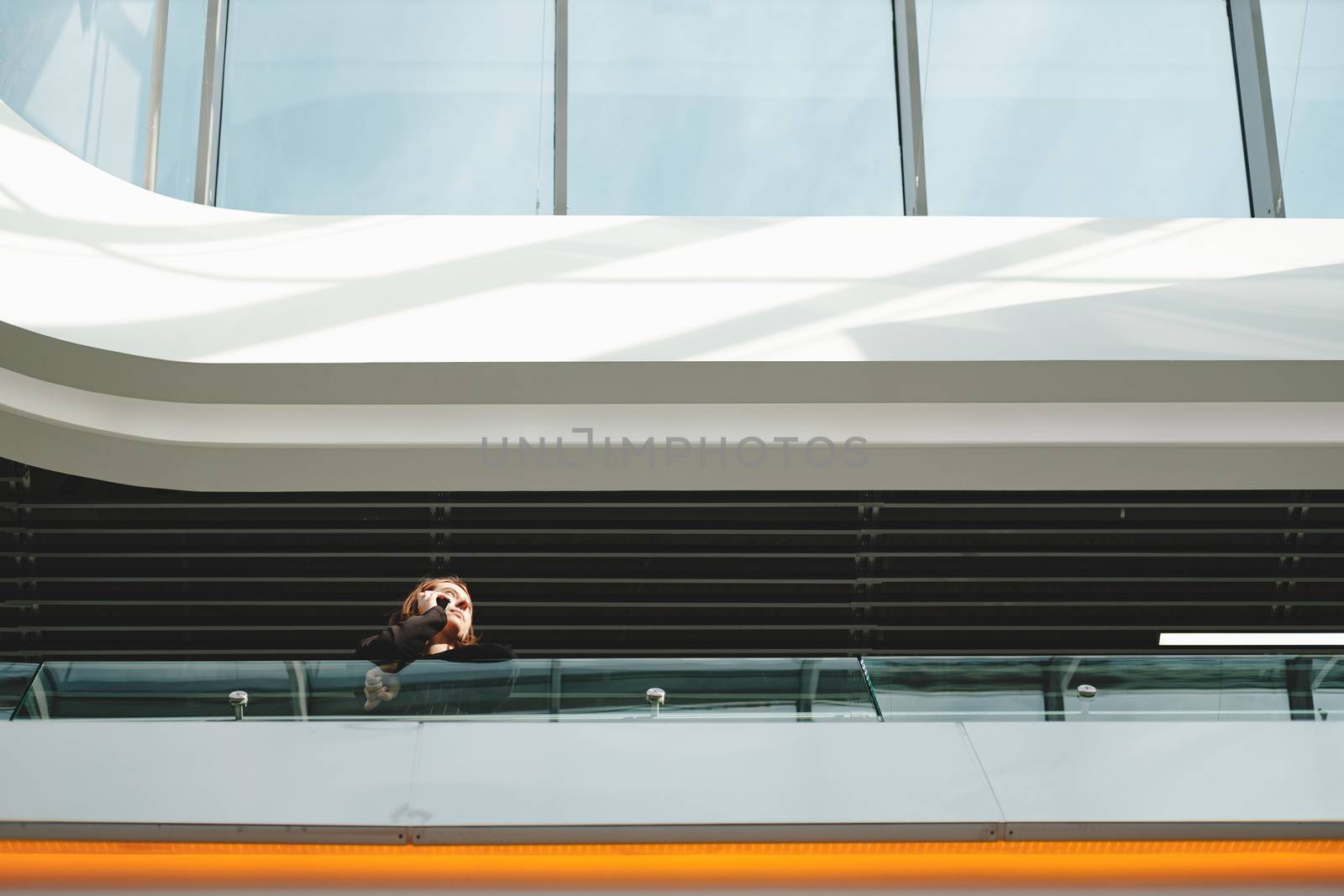 Woman talks on the phone at public place. Young female adult using smartphone at a shopping mall or airport, view from below