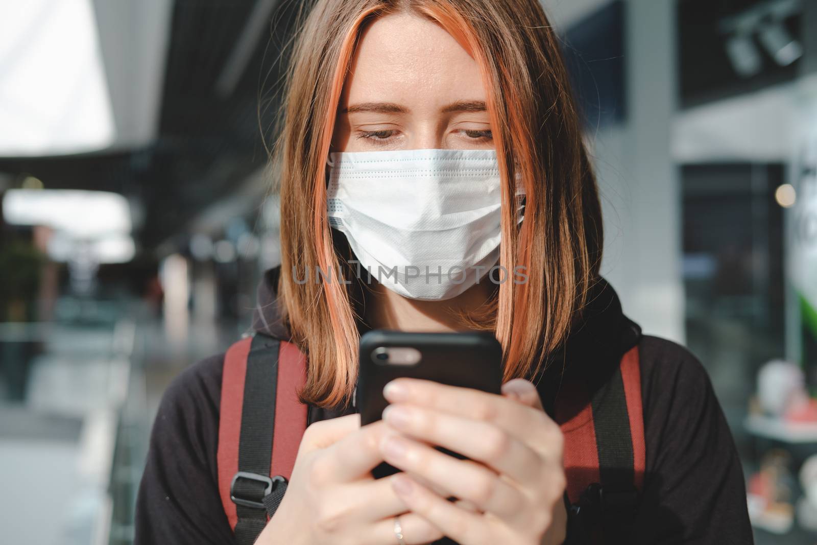 Woman in protective face mask using the phone at a public place. by photoboyko