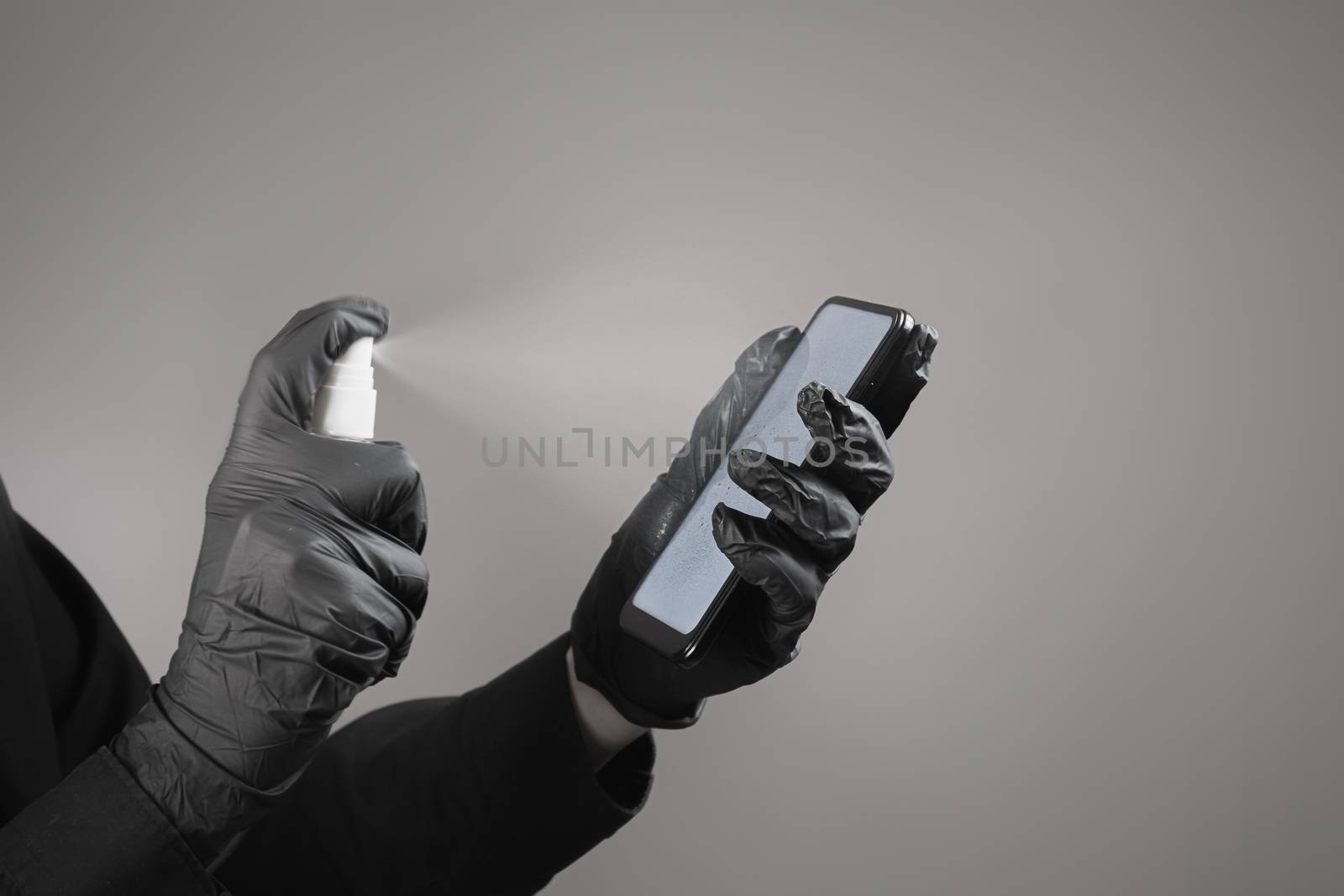 Cleaning the phone with a sanitizer, total black concept. Hands in black gloves spray sanitizer on the smartphone screen. Virus spread prevention concept