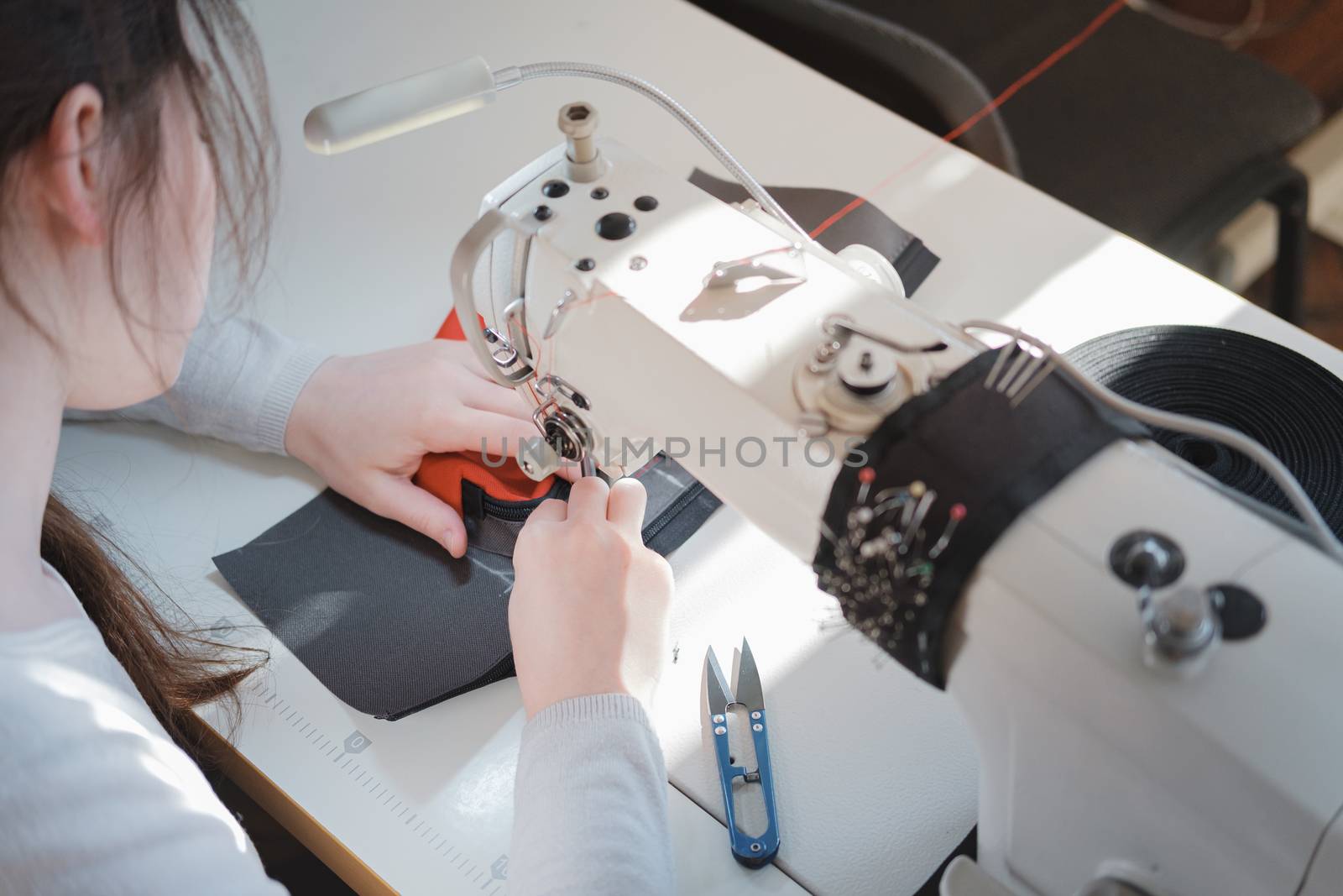 Seamstress at her work place, shoulder view. Needlewoman at overlock sewing machine doing professional work, concept of labor