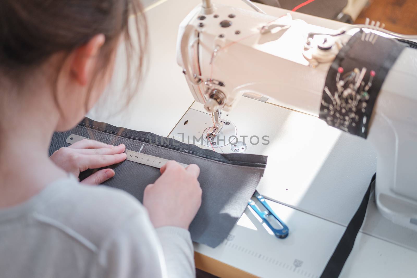 Seamstress measuring piece of fabric, shoulder view. Needlewoman at overlock sewing machine doing professional work, concept of labor