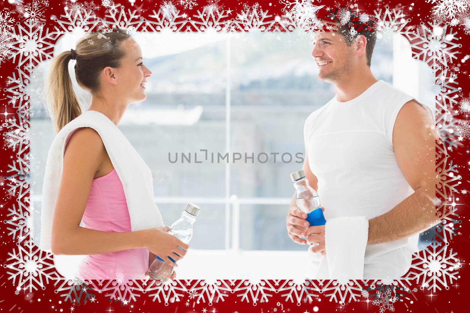 Fit couple holding water bottles and towels in exercise room against snow