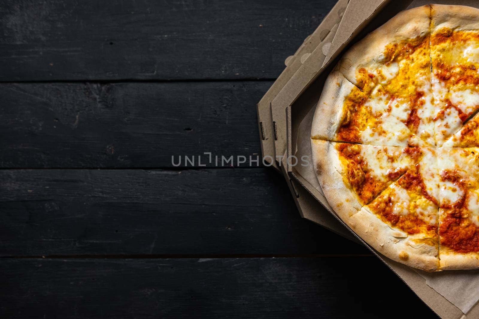 Pizza margherita in an open delivery box, dark backdrop with text space. Delivery foods, takeaway food concept: pile of pizza boxes on black wood background