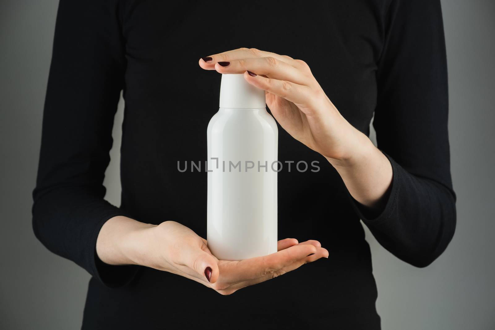 Generic white bottle in female hands against low light backdrop. by photoboyko