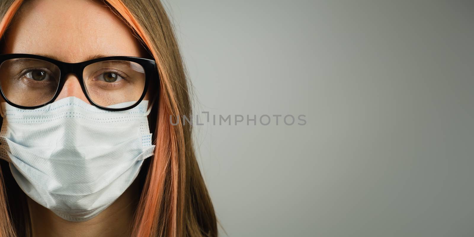 Intelligent woman in eyeglasses wearing medical mask, copy space banner. Young female in surgical mask in dark gray backdrop. Concept of personal hygiene, protection against virus and germs or professional gear