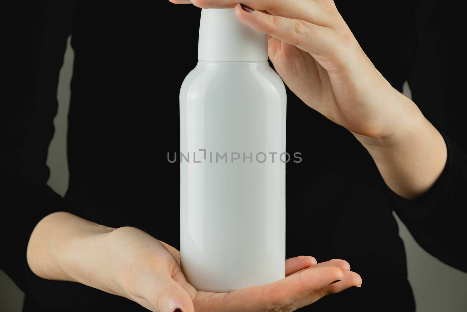 Generic white bottle in female hands against low light backdrop. by photoboyko