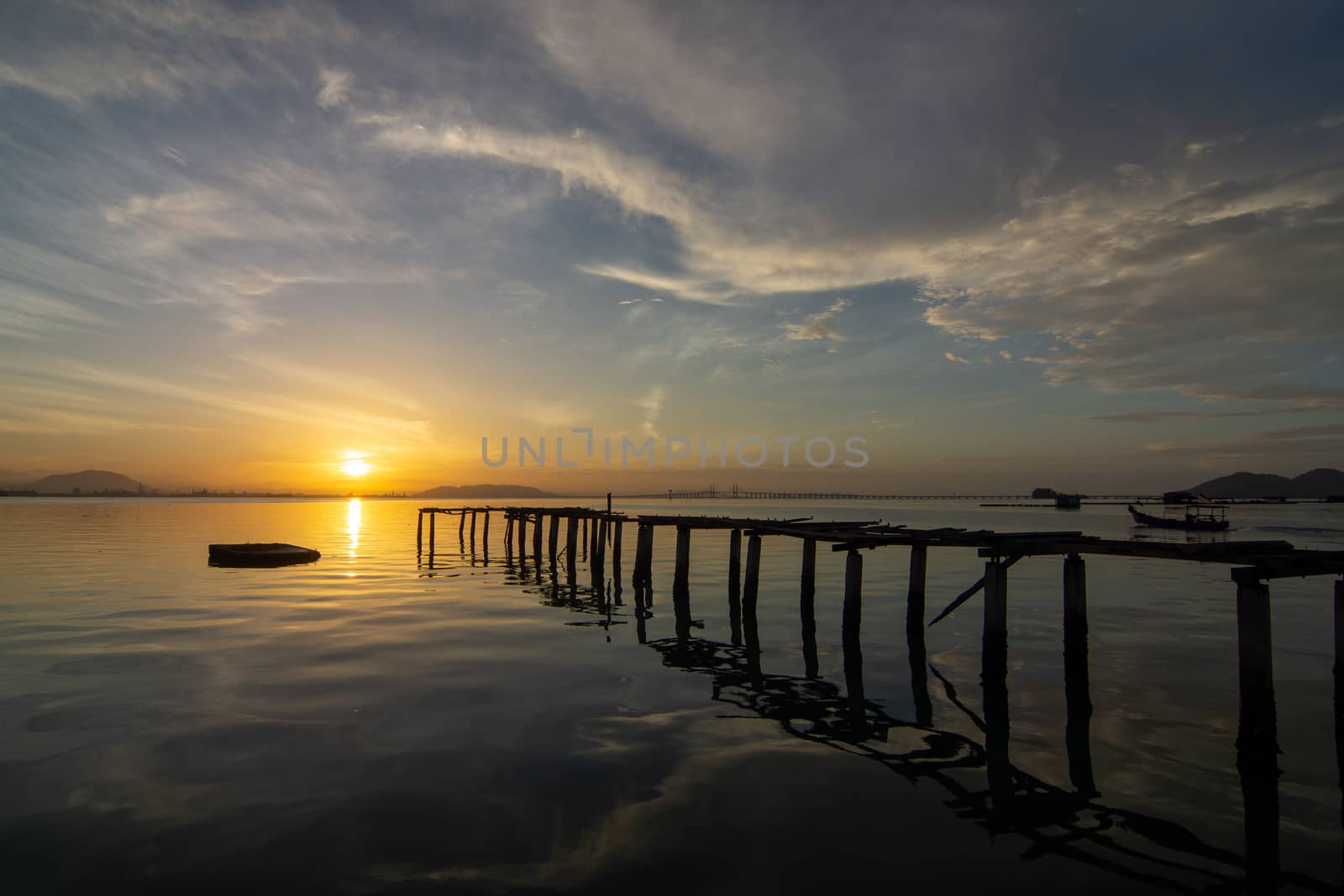 Landscape reflection of wooden bridge on sea in early morning at fisherman pier Jelutong, Penang. Penang Bridge at background.