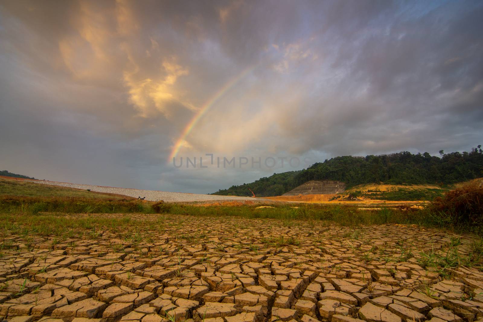 Crack dry land in Mengkuang dam, Penang, Malaysia during drought period. A rainbow in appear at background.