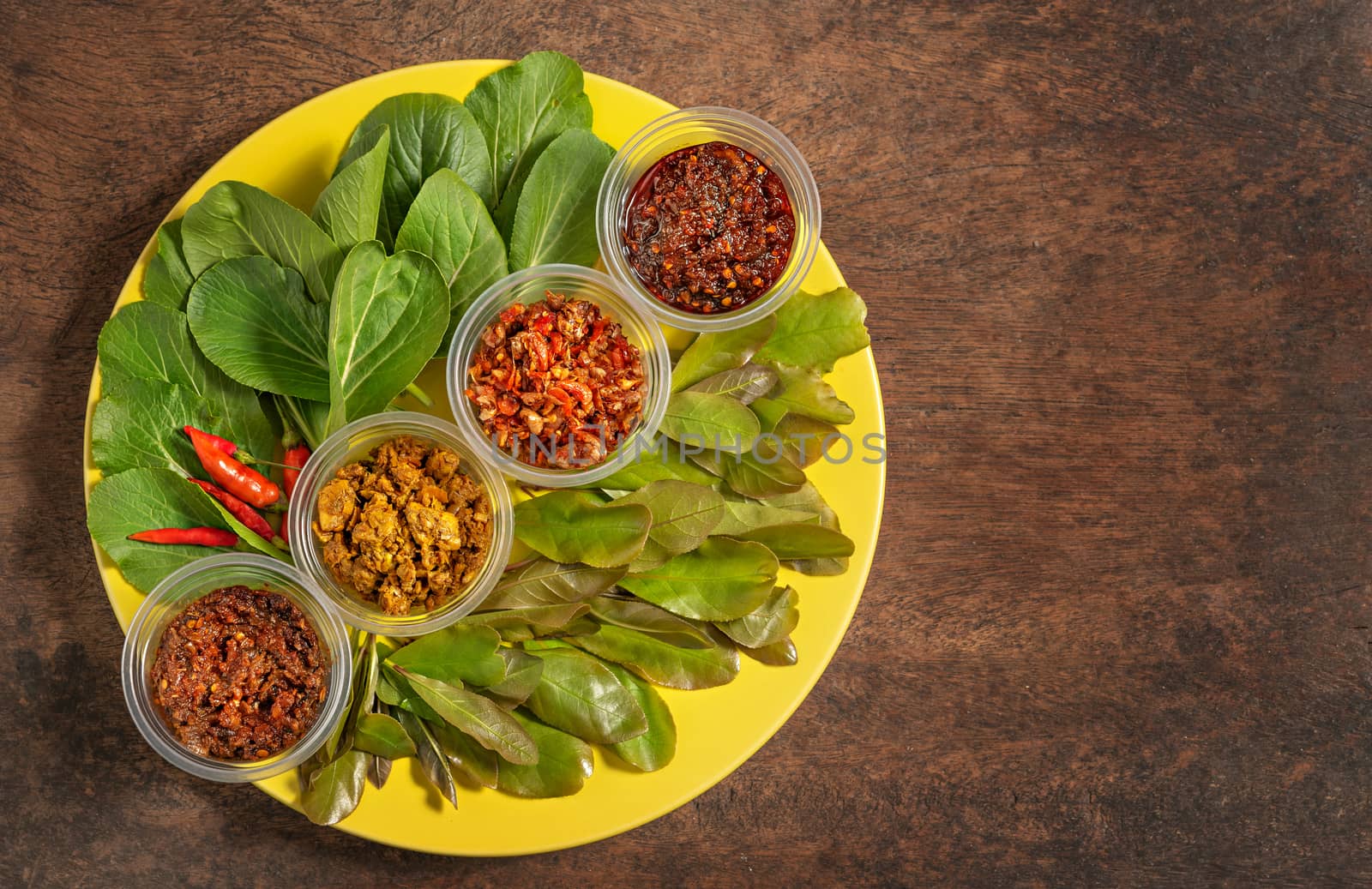 thai style chili paste served with fresh vegetables on yellow plate over wooden background