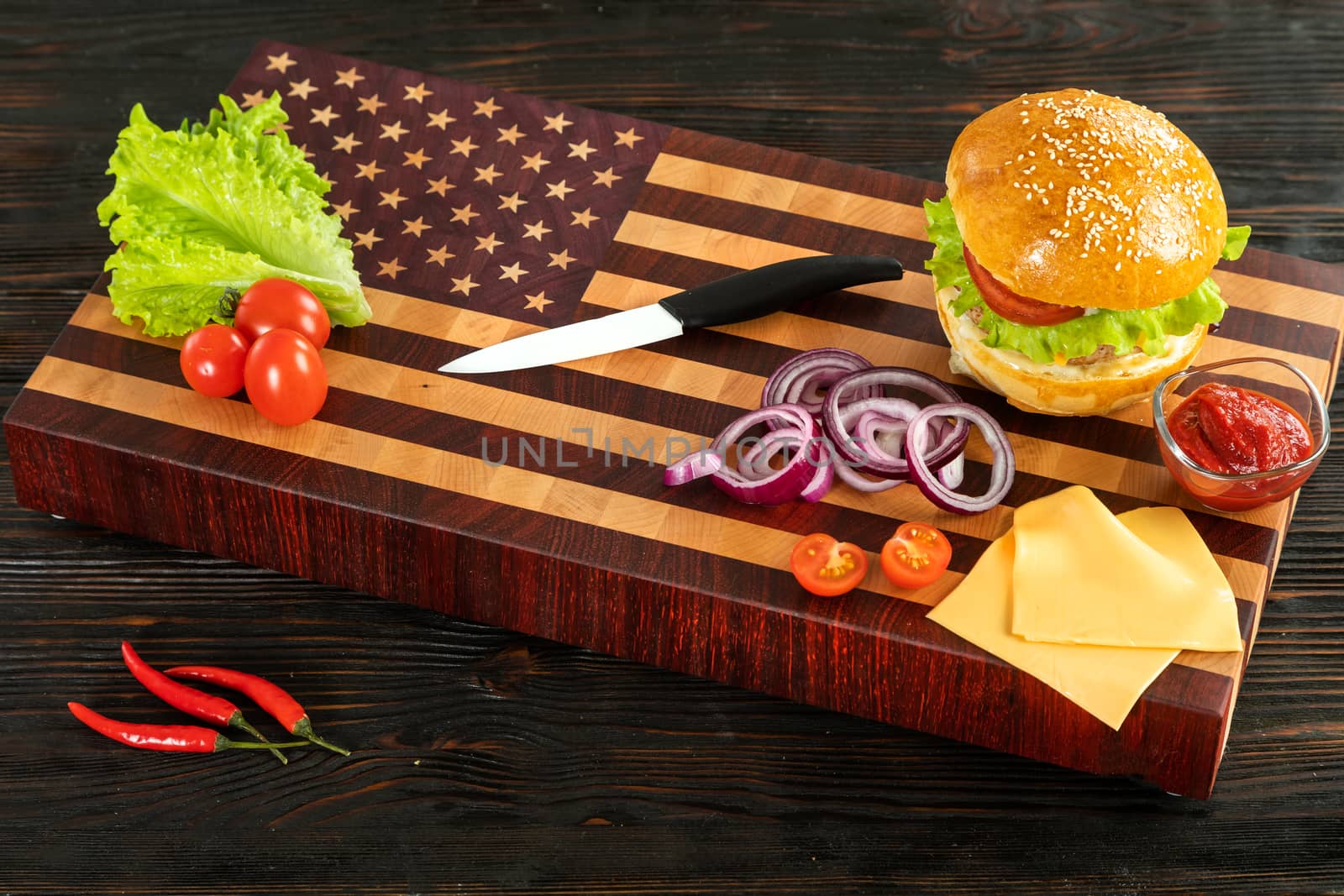 Burger next to vegetables and cheese on a wooden cutting board