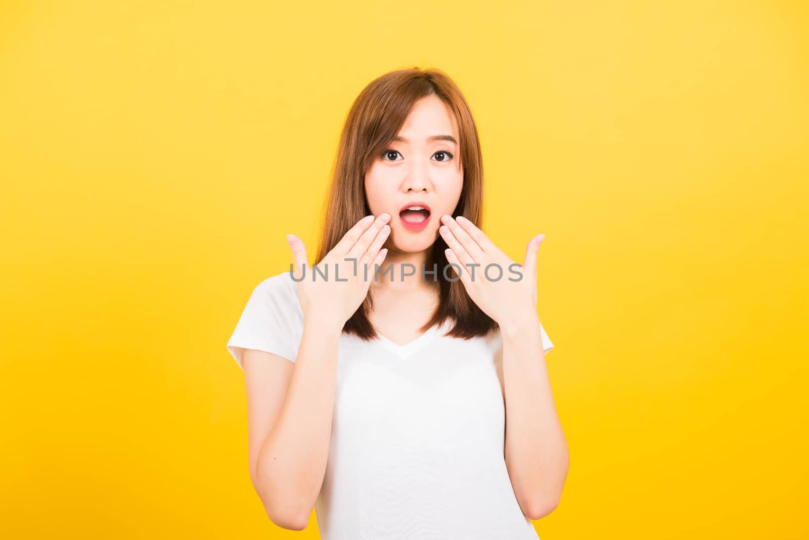 Asian happy portrait beautiful cute young woman teen standing amazed, shocked afraid wide open mouth eyes gesturing palms looking to camera isolated, studio shot on yellow background with copy space