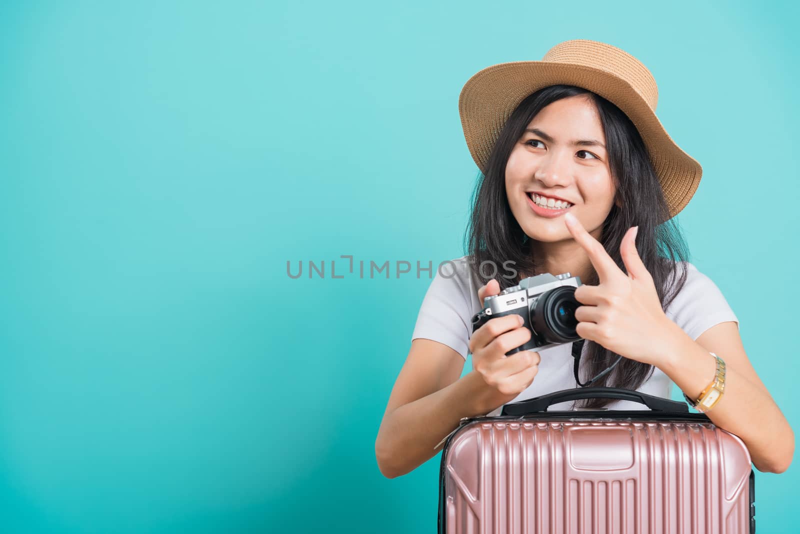 Traveler tourist happy Asian beautiful young woman sitting wear white t-shirt, holidays travel concept, her holding suitcase bag and photo mirrorless camera, shoot photo in studio on blue background
