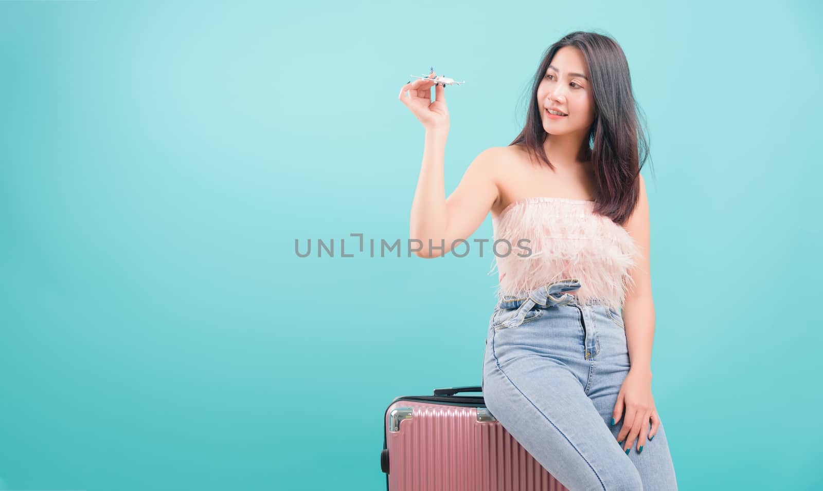 Asian happy portrait beautiful young woman standing smile in summer trip to travel, hat with a suitcase bag on blue background with copy space for text, Traveler tourist concept