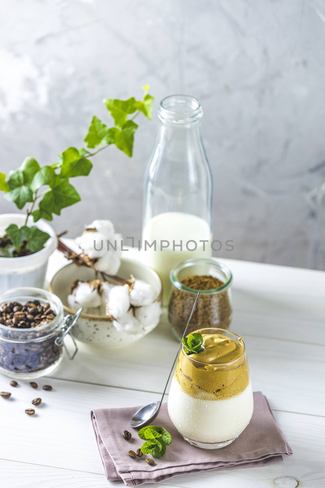 Glass of Iced Dalgona Coffee, a trendy fluffy creamy whipped coffee, decorated by mint and ingredients on light rustic background, copy space.