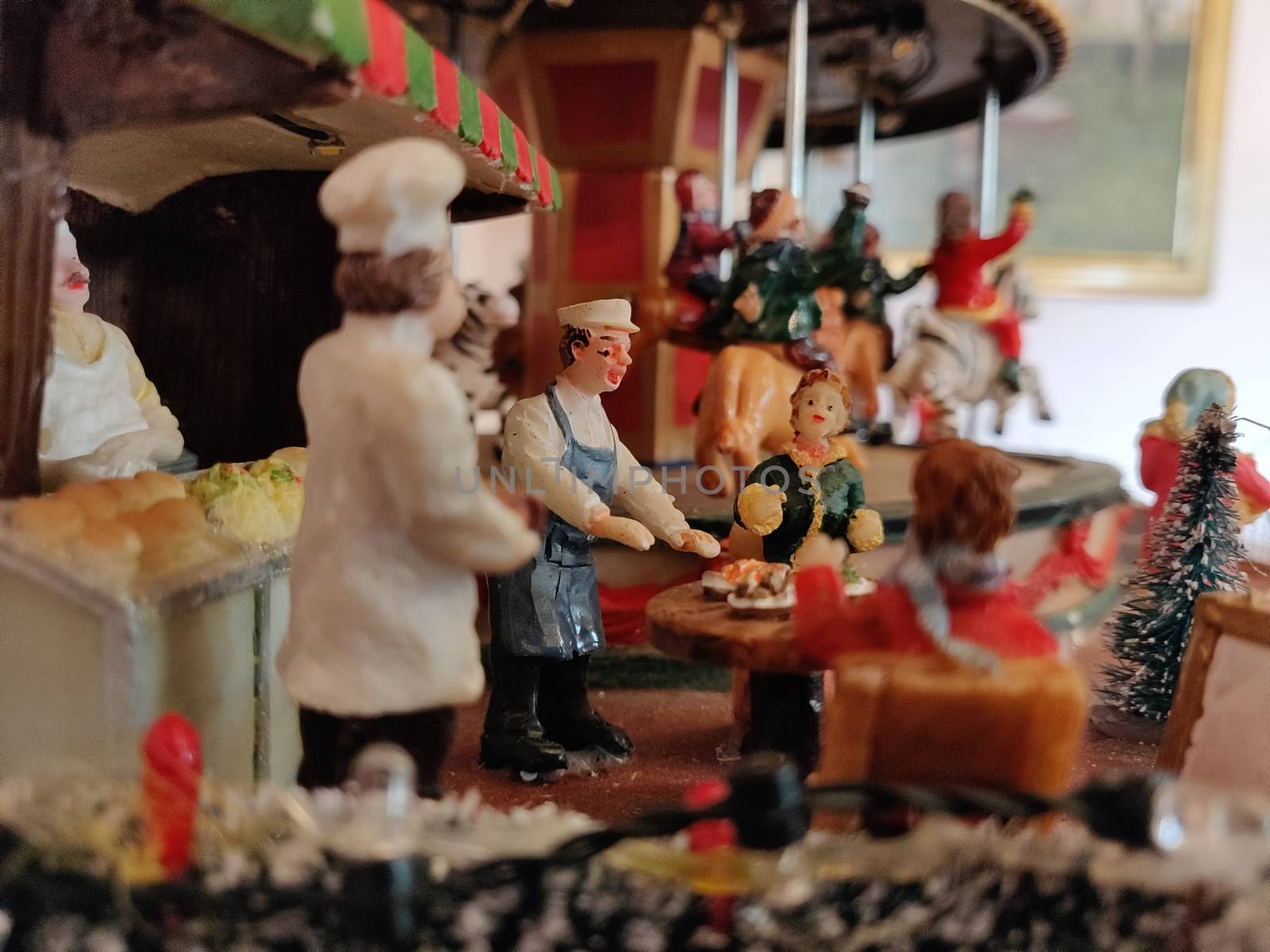 A doll and miniature sculpture of a carnival scene with carousal in the background. The doll is serving the customers