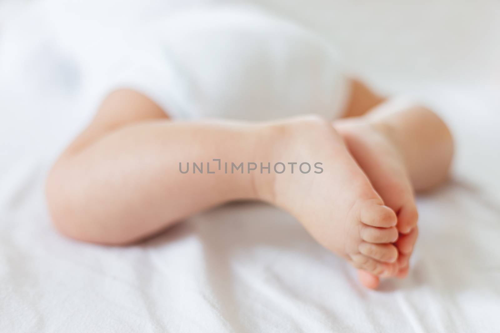 Baby's feet. Bare heels of little child wearing white bodysuit and diaper. Cozy morning bedtime at home. by aksenovko