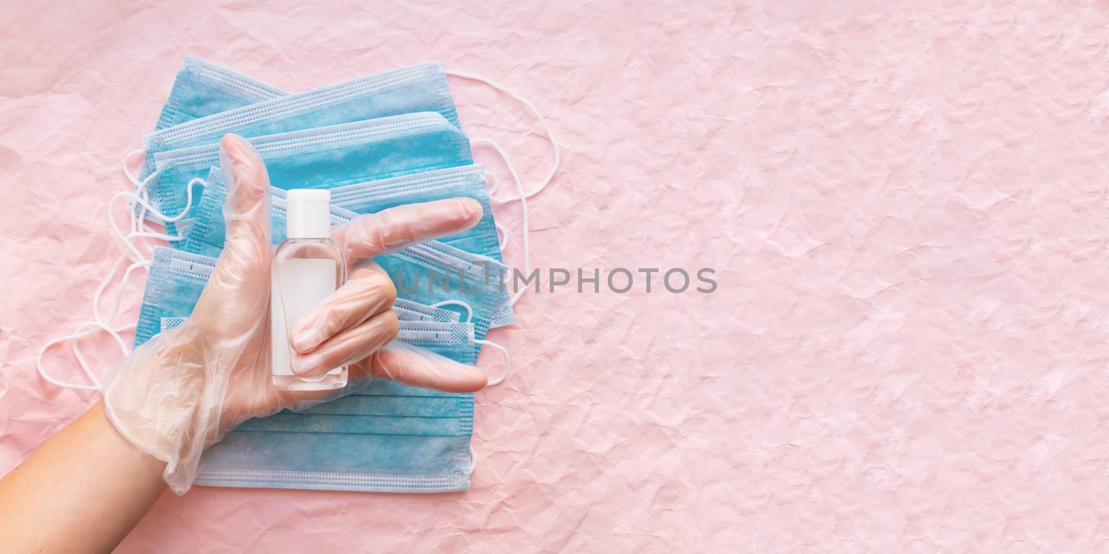 Top view on hand in protective gloves with medical masks and sanitizer in transparent bottle. Woman make victory gesture. Coronavirus COVID-19 concept on pink crumpled background with copy space.