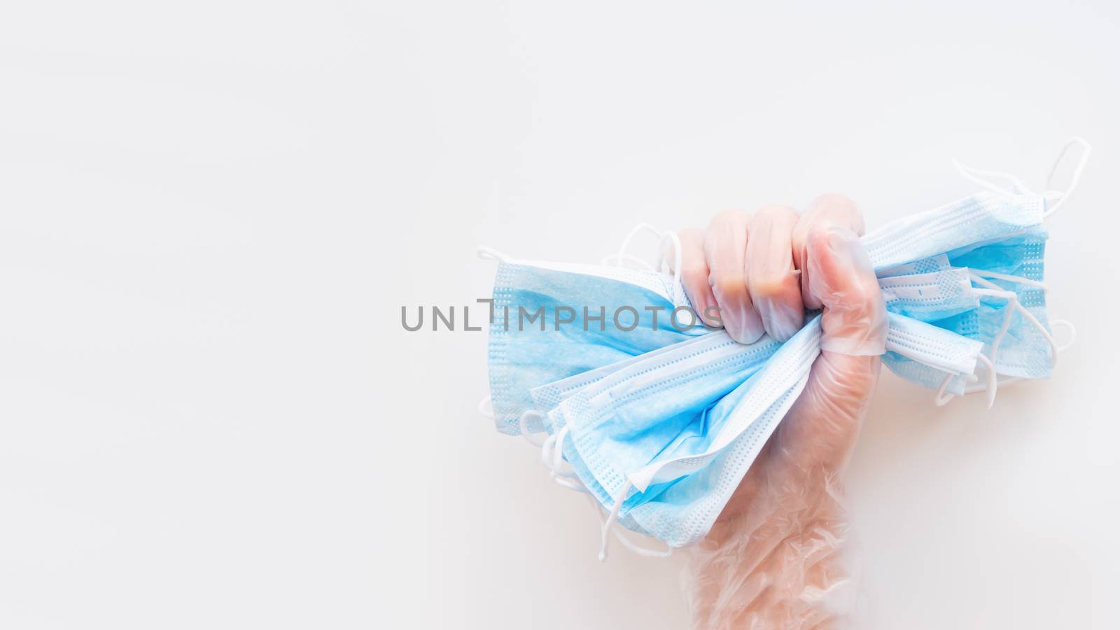Top view on doctor's hand grasping pack of blue protective medical masks. Coronavirus COVID-19 concept on white background with copy space.
